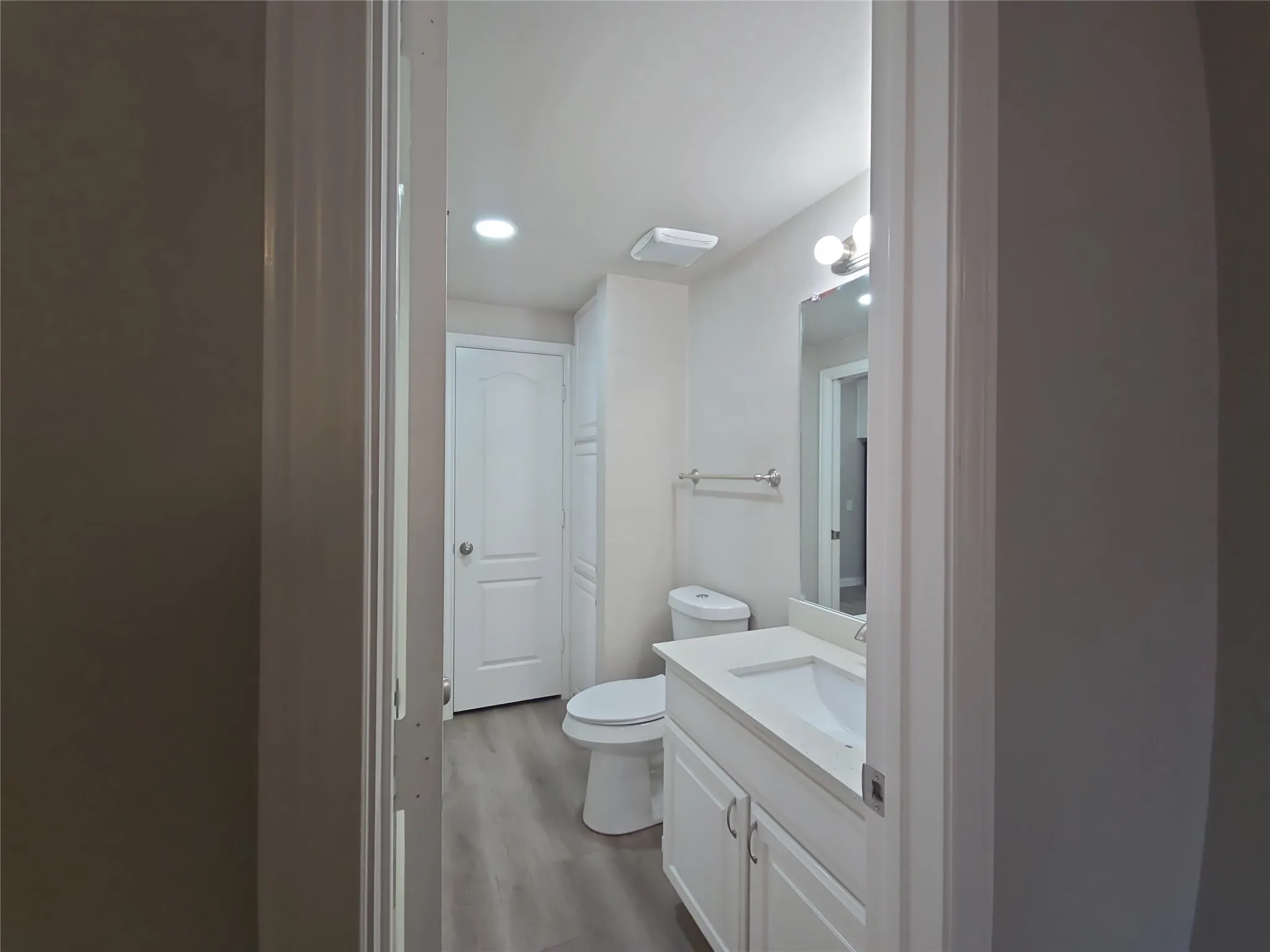 Bathroom featuring a white vanity with integrated sink, white cabinetry, wall-mounted mirror, and wood-finish flooring