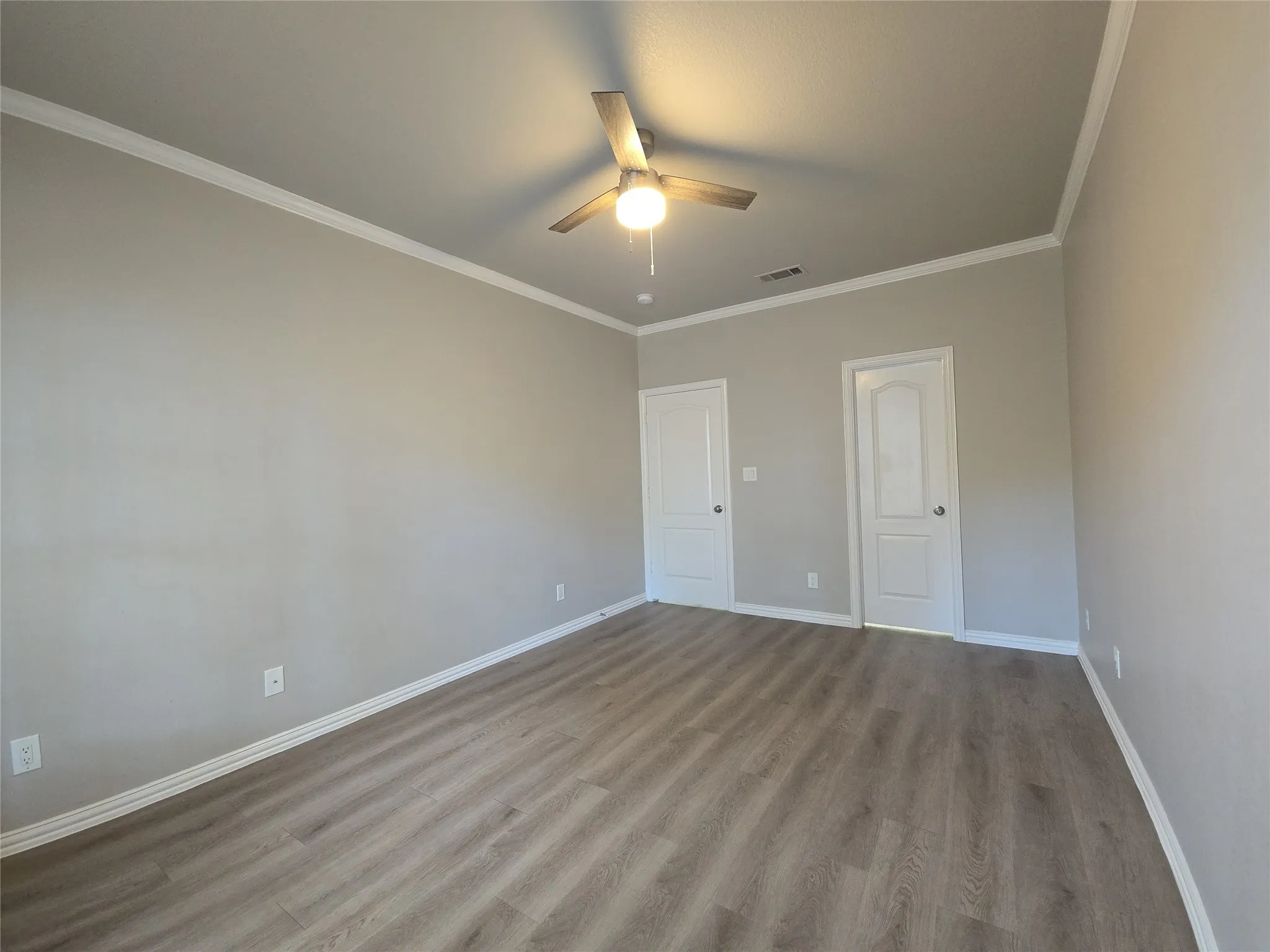 Wood-finish flooring, crown molding, ceiling fan with integrated lighting, and two panel doors