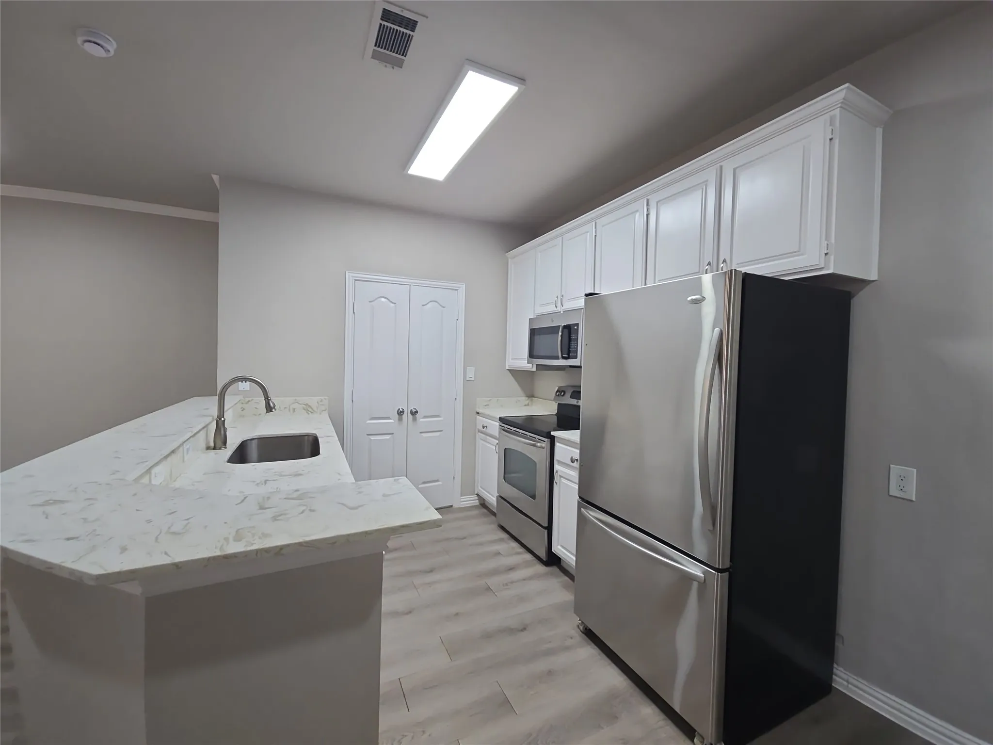 Kitchen featuring white cabinetry, stainless steel appliances, light-toned countertops, and wood-finish flooring