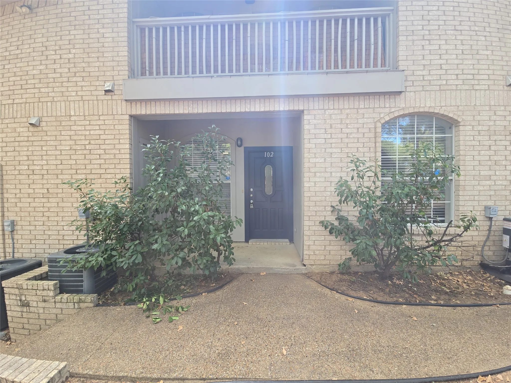 Brick exterior featuring an arched window, a privacy balcony, and a dark entry door with decorative glass