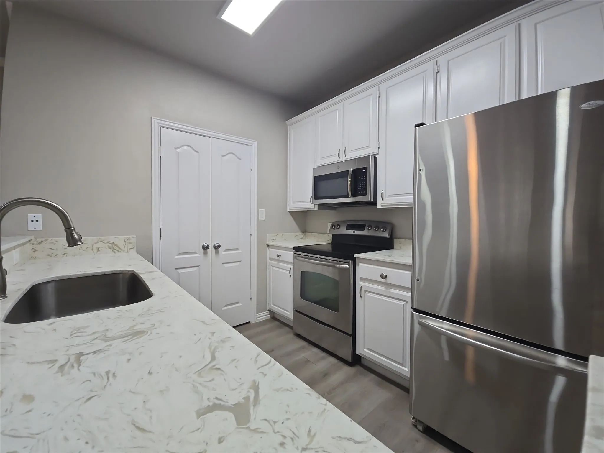 Kitchen featuring white cabinetry, light-toned countertops, stainless steel appliances, and wood-finish flooring