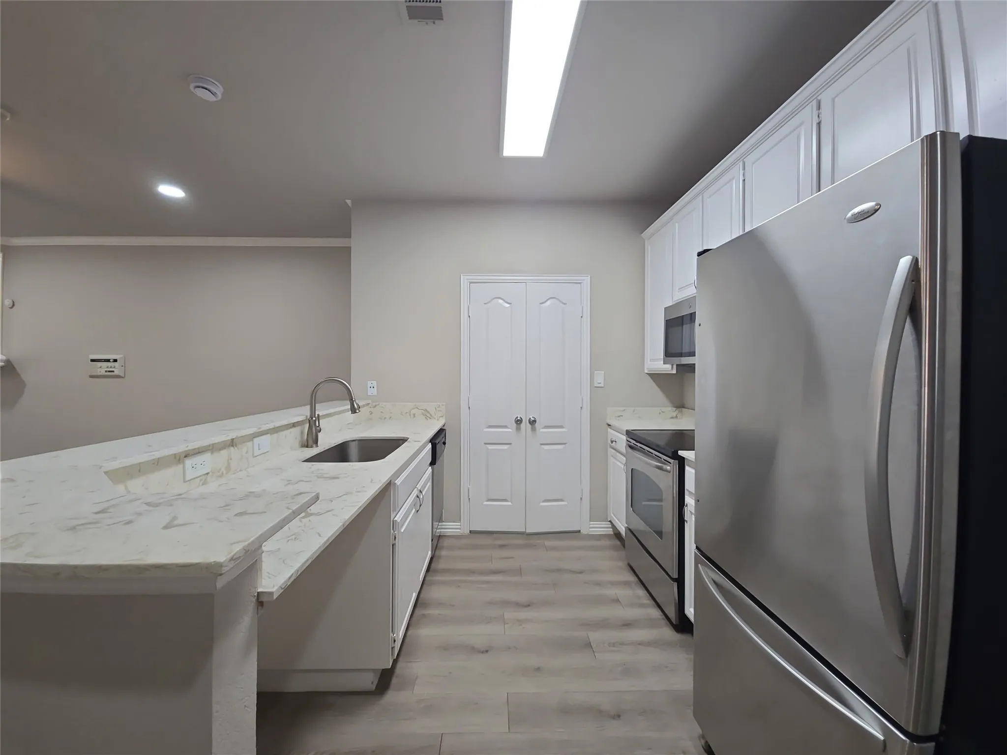 Kitchen featuring wood-finish flooring, white cabinetry, integrated stainless steel appliances, and a double-basin sink with a gooseneck faucet