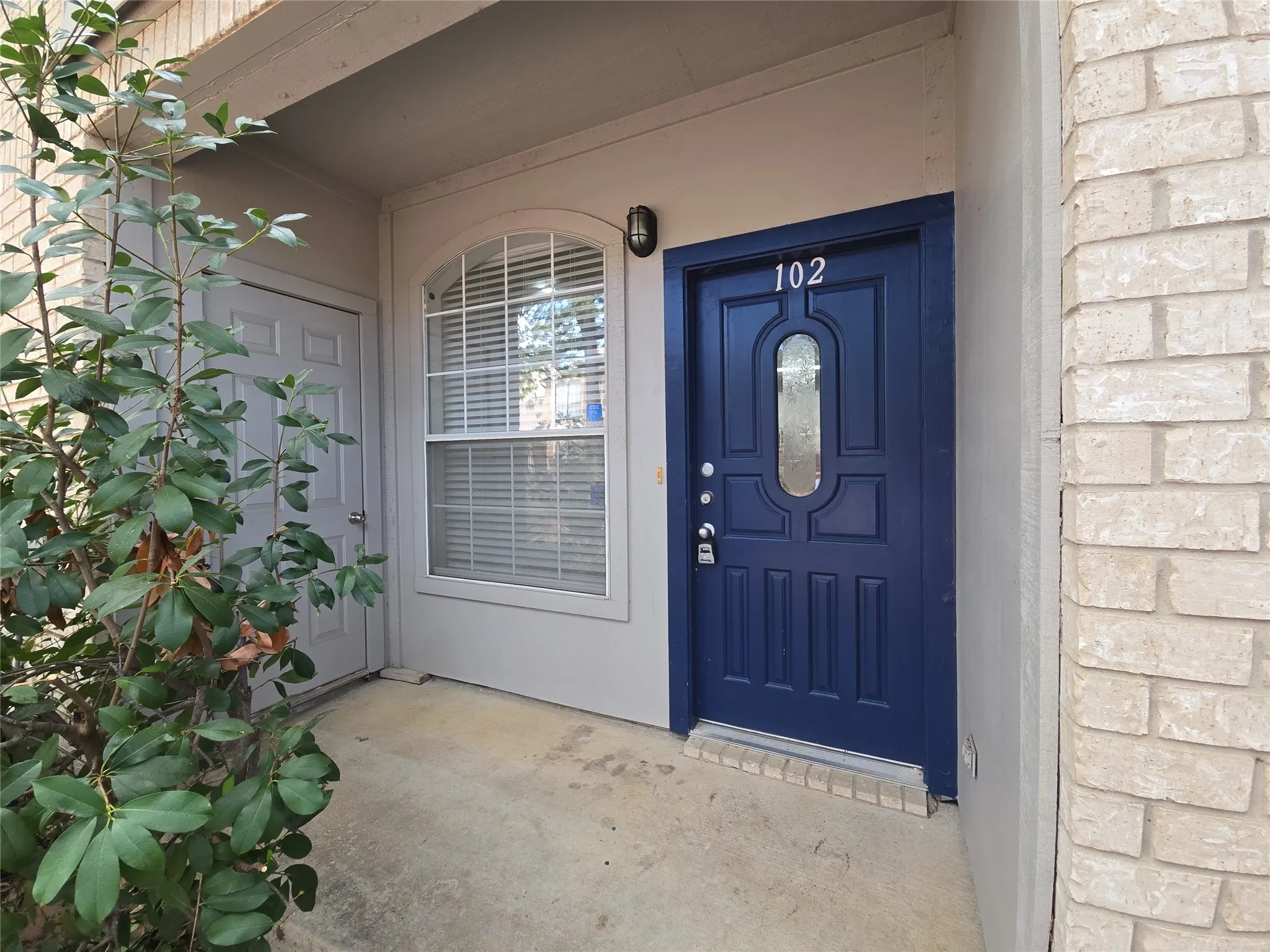 Entryway featuring a paneled door with decorative glass, an arched window with blinds, and light-colored brick siding