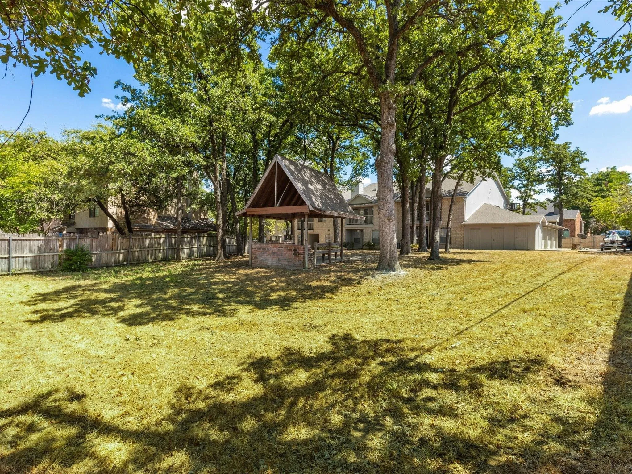 Expansive grassy yard with mature trees, a wood-framed gazebo, and perimeter fencing