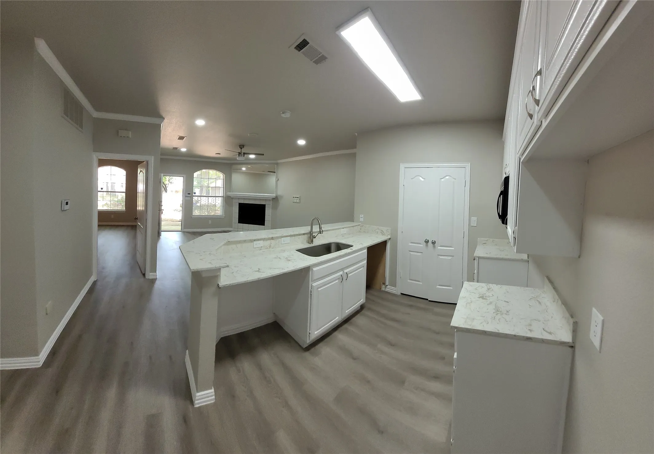 Open-concept kitchen featuring white cabinetry, light-toned countertops, and wood-finish flooring