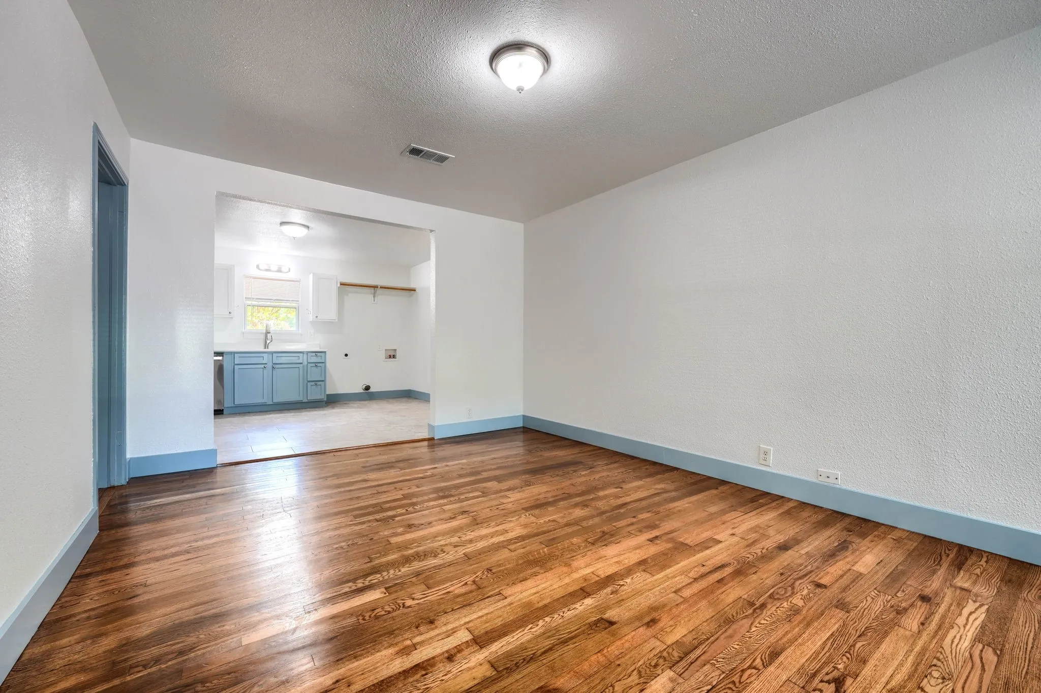 Wood-finish flooring with a smooth finish, white walls, and a ceiling-mounted light fixture