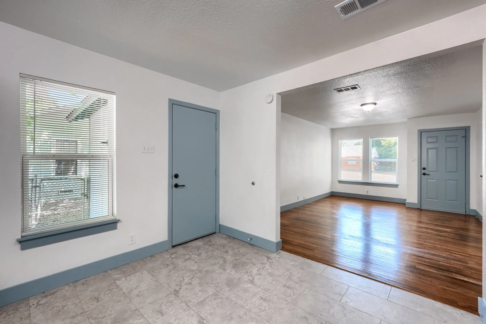 Tiled flooring, interior doorway with matte black hardware, window with horizontal blinds, recessed lighting, and wood-finish flooring in an adjoining room