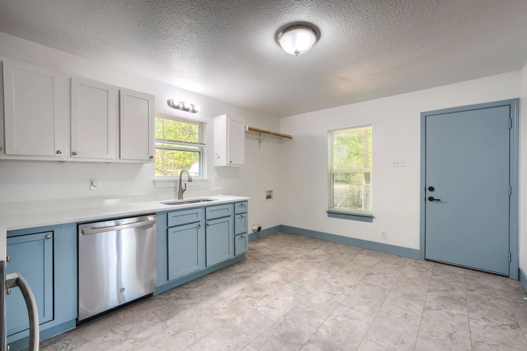 White upper cabinetry complemented by blue lower cabinetry, stainless steel dishwasher, and a stainless steel sink with a gooseneck faucet