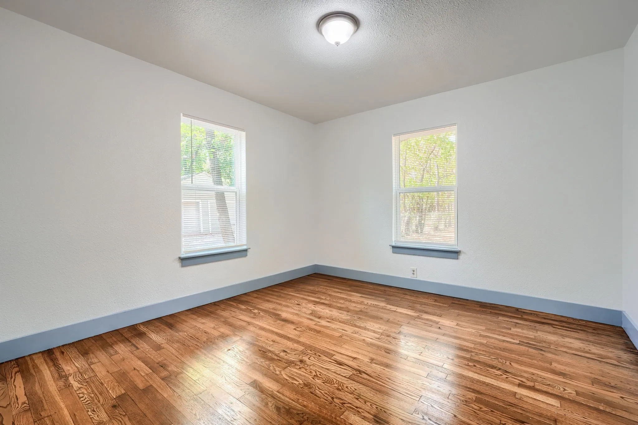 Hardwood flooring, white painted walls, two windows, painted window sills, and a ceiling-mounted light fixture