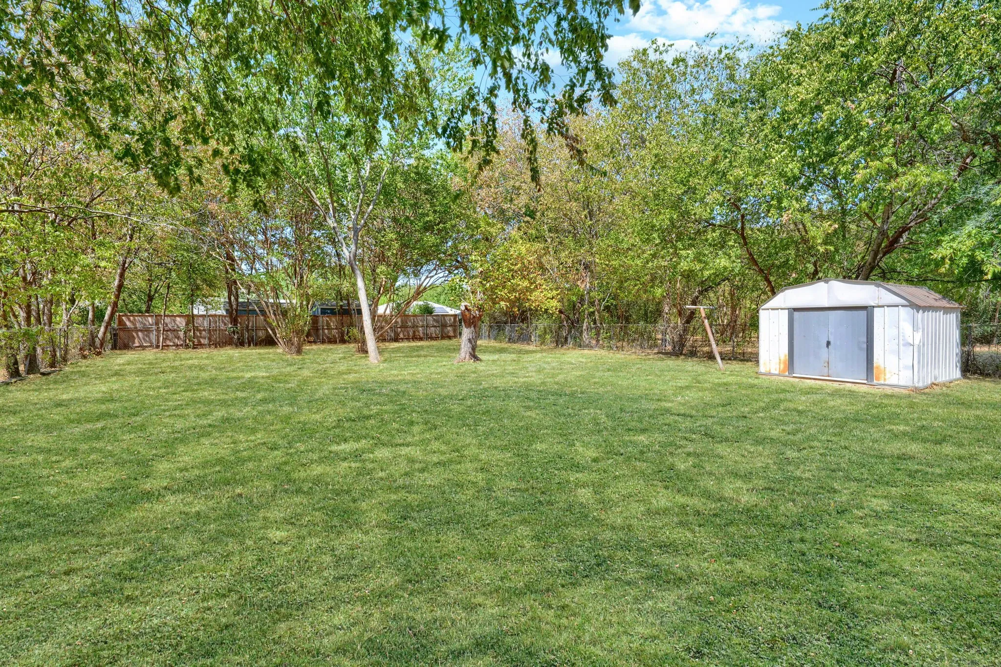 Expansive lawn area, mature trees, wood fence perimeter, and a detached storage shed
