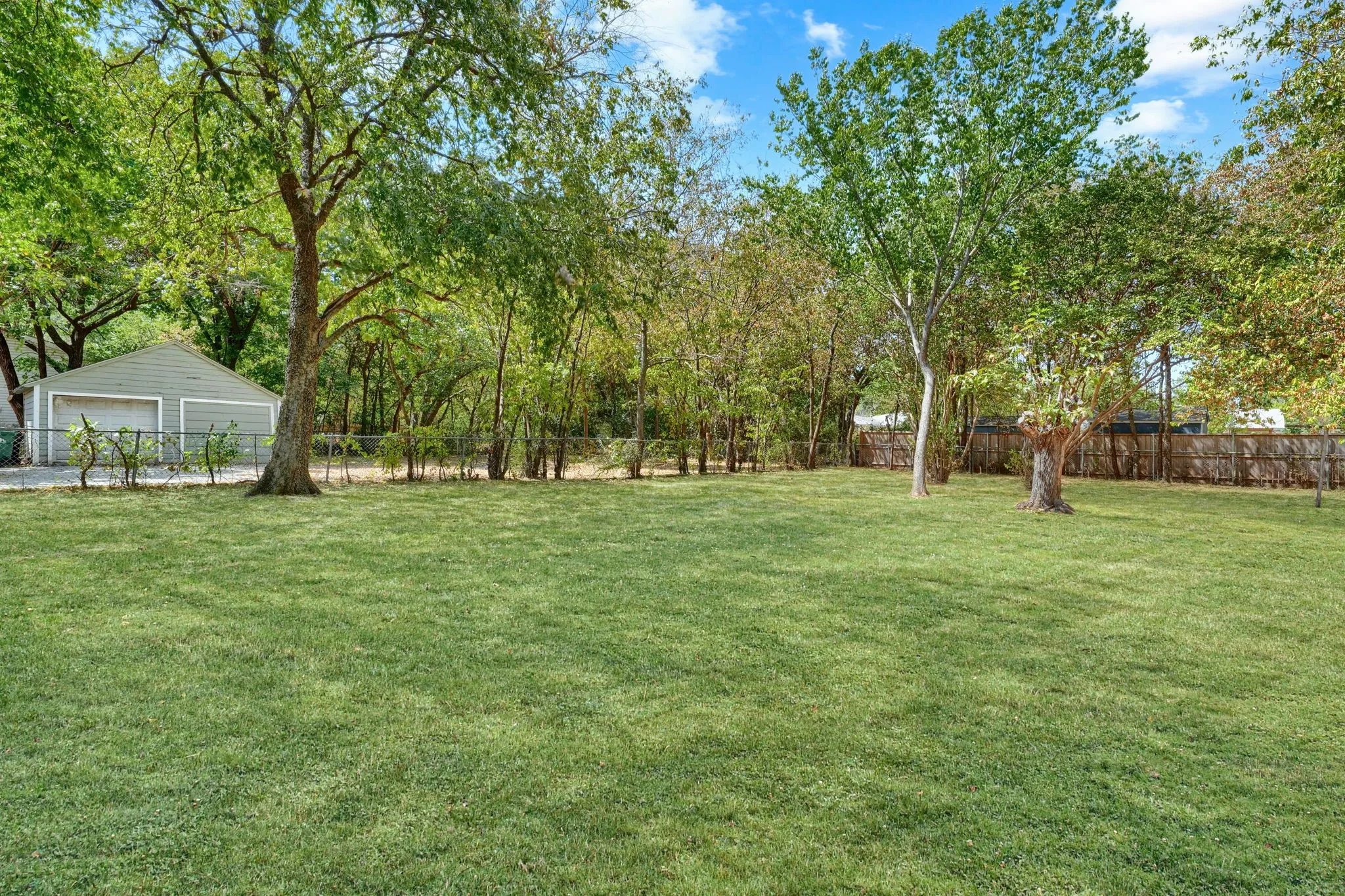 Expansive green lawn with mature trees and a detached two-car garage