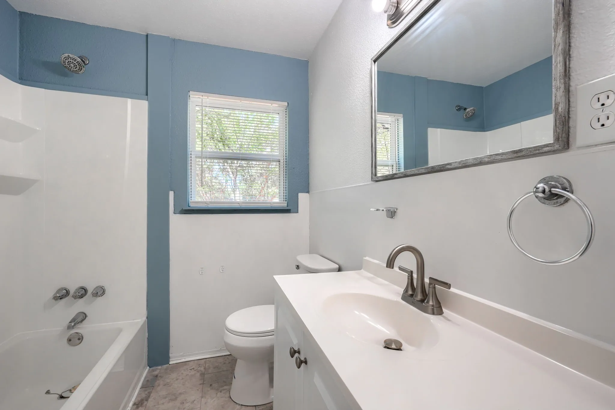 Integrated tub and shower combination, single vanity with integrated sink, brushed nickel faucet, framed mirror, and window with blinds