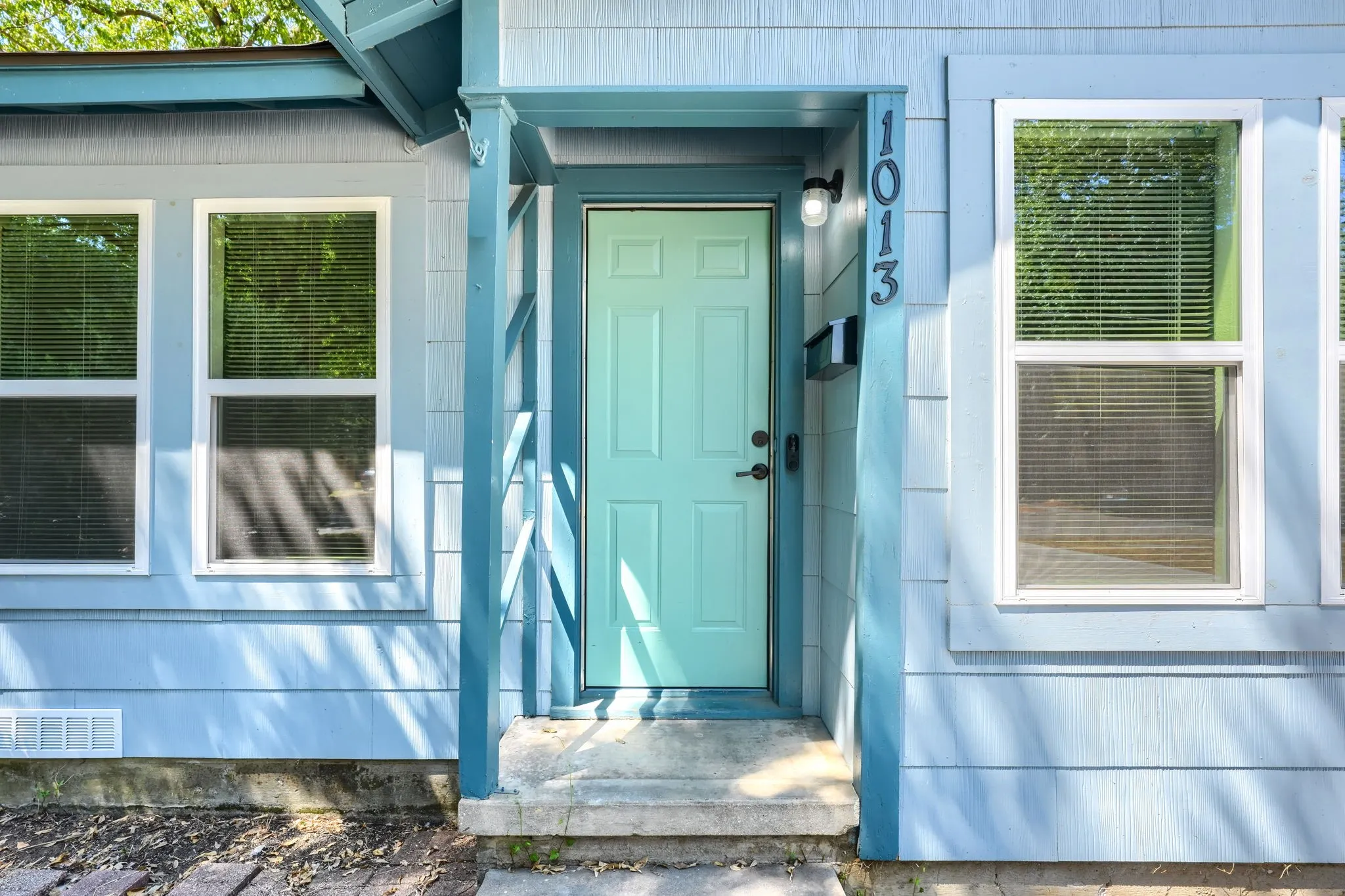 Light blue siding exterior with white-framed windows, a mint green entry door, and a black wall-mounted light fixture