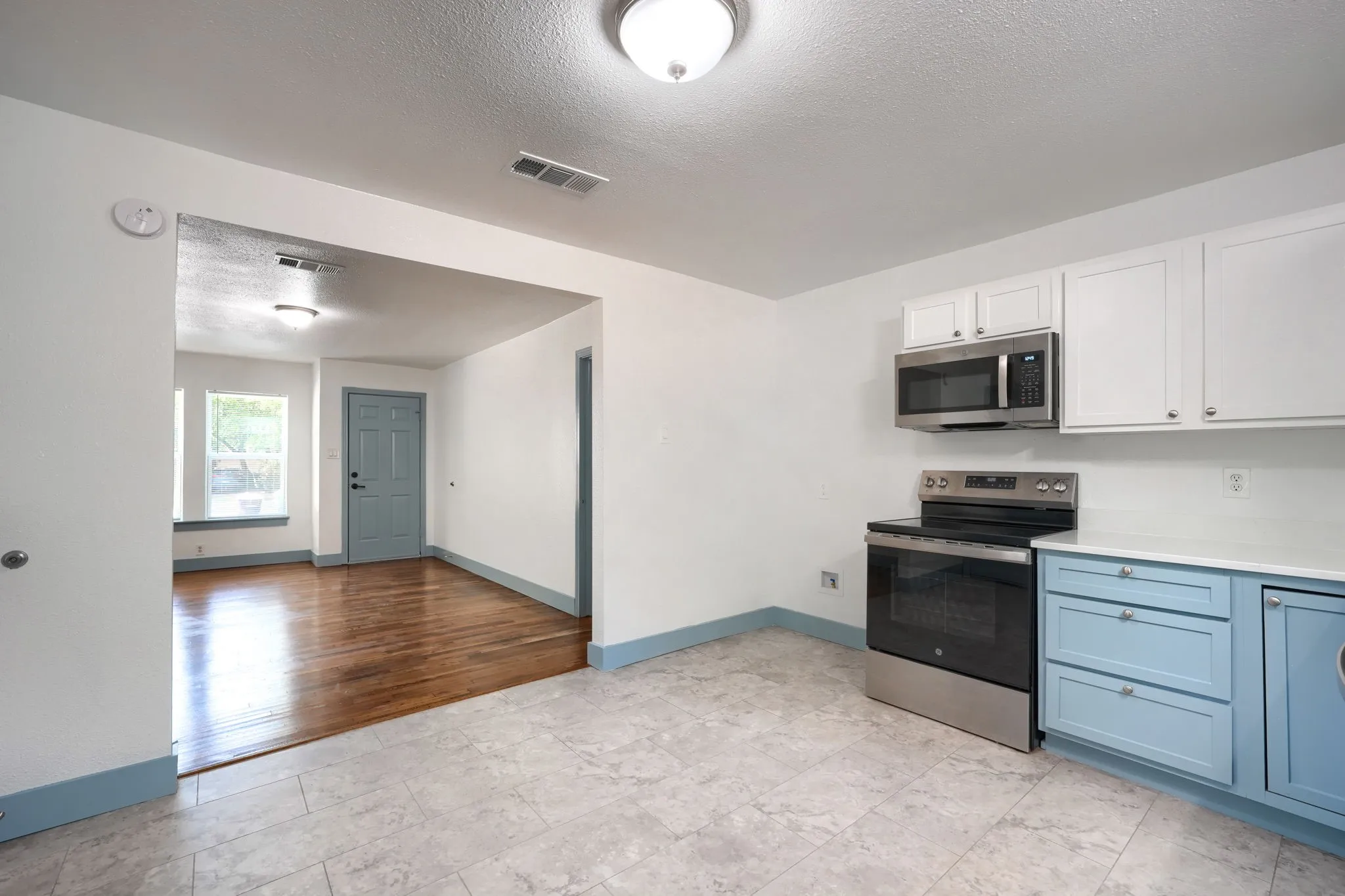 Kitchen featuring stainless steel appliances, white upper cabinetry, blue lower cabinetry, white countertops, and tile flooring