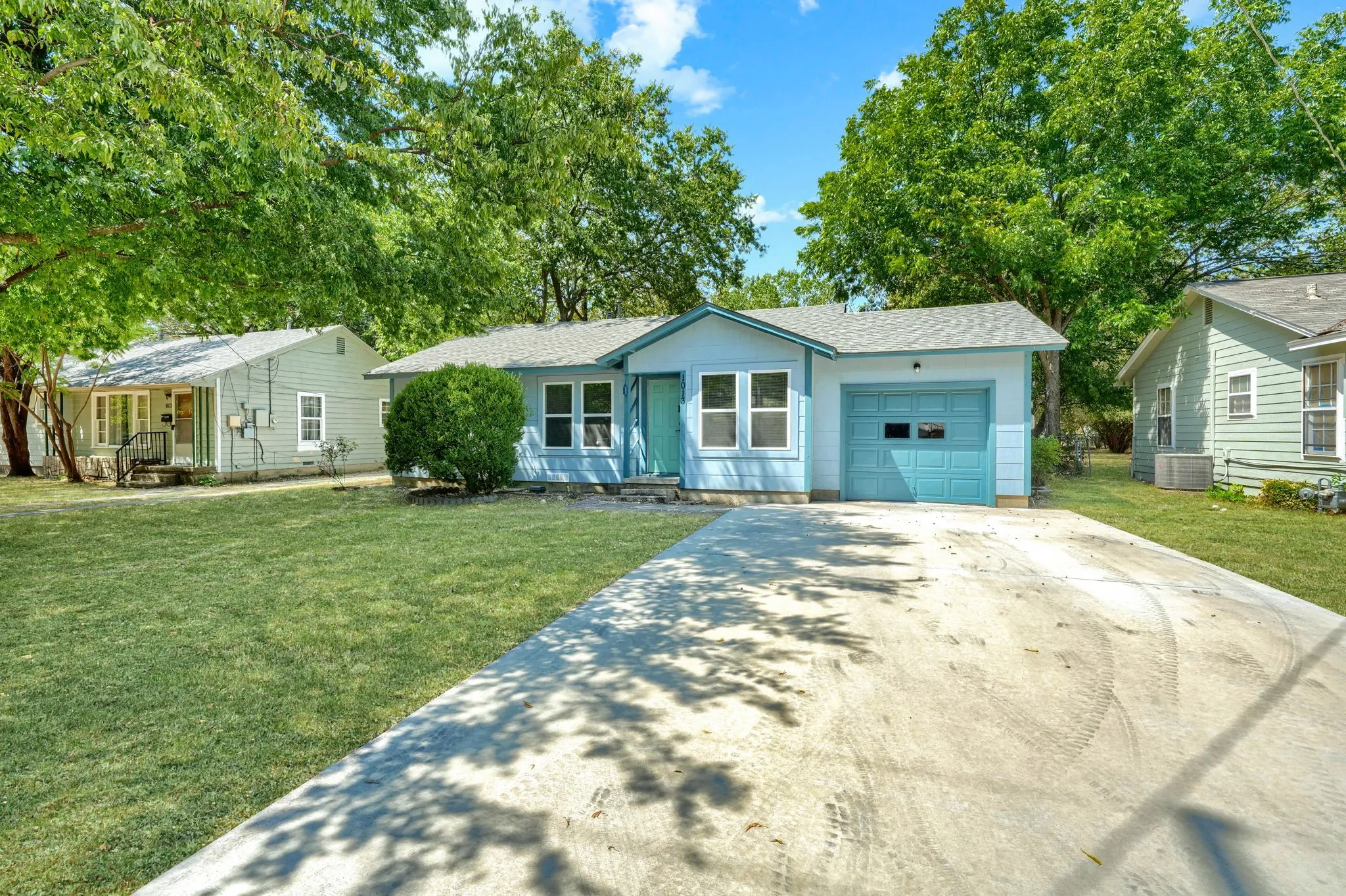 Light blue exterior siding, white window trim, attached garage with a blue garage door, concrete driveway, and front lawn