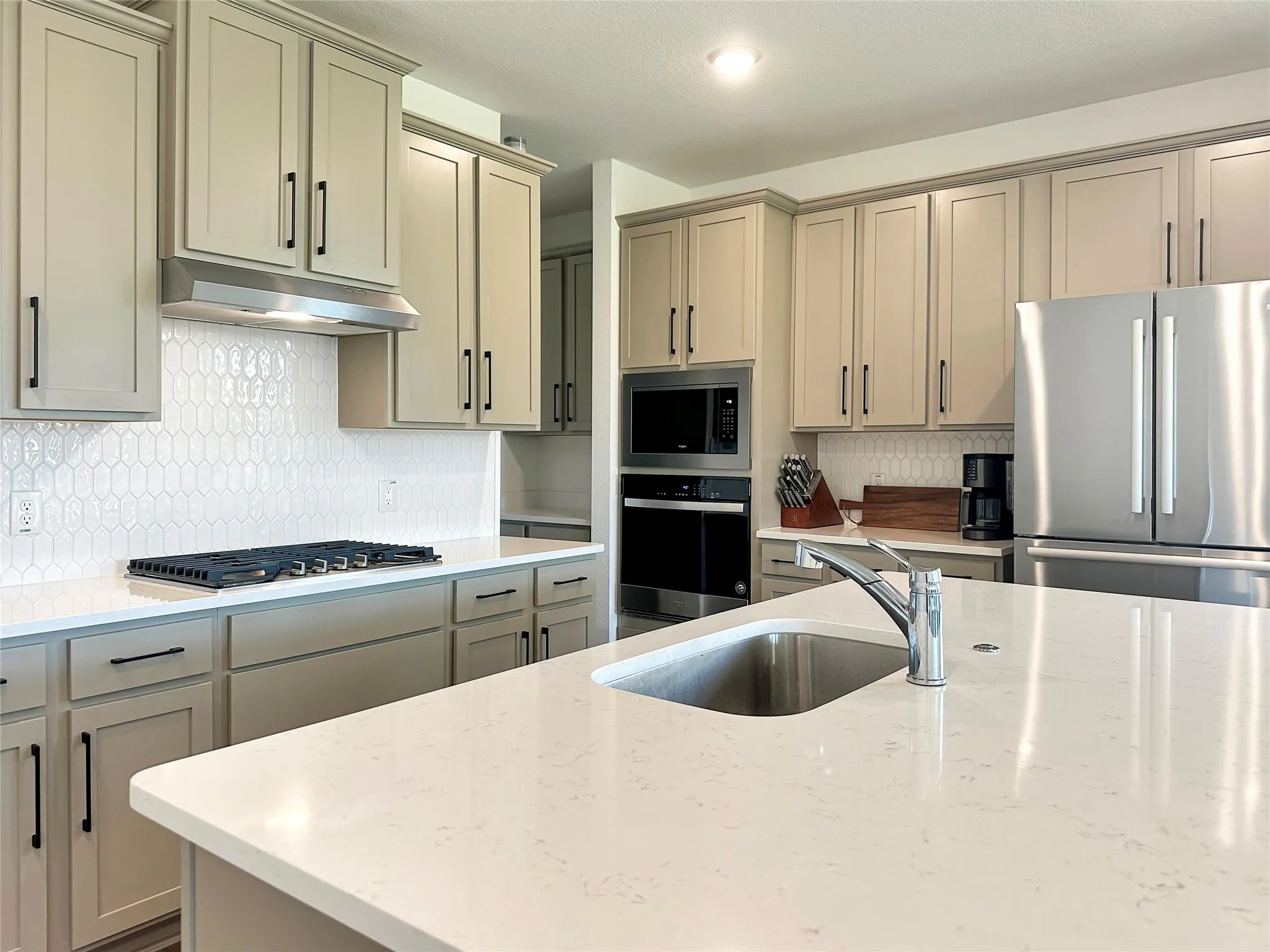 Kitchen with appliances with stainless steel finishes, light stone counters, backsplash, and sink