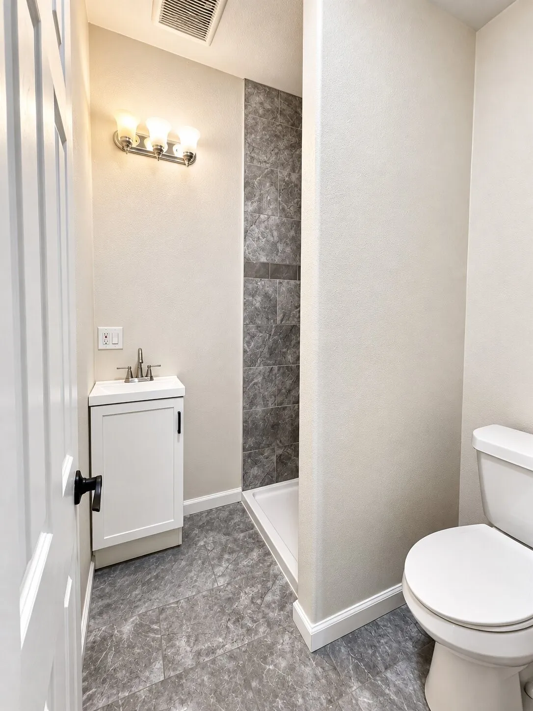 Compact bathroom featuring a shower stall with gray tiled walls, a white vanity with integrated sink, and gray-toned floor tiling