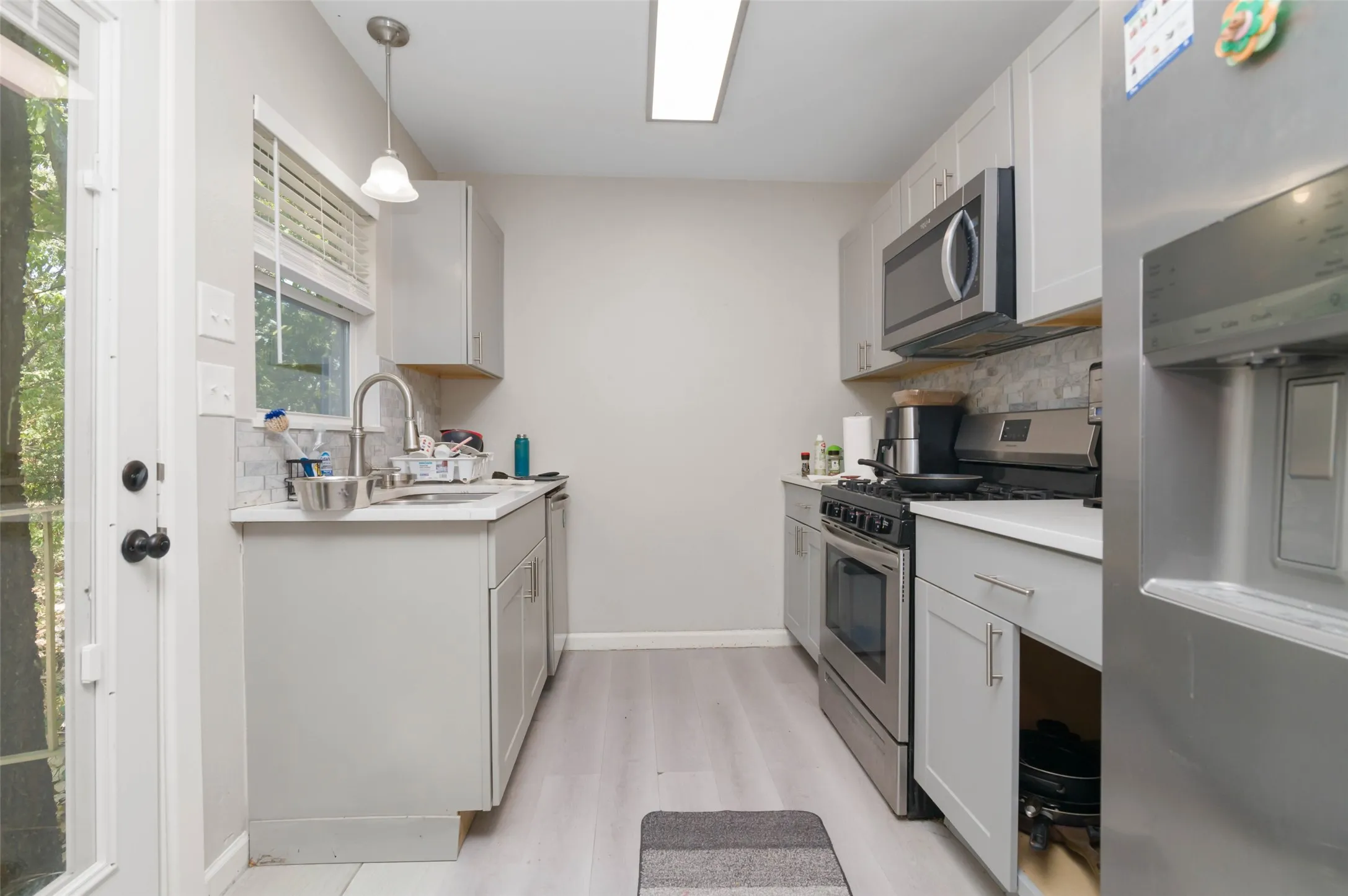Galley kitchen featuring light gray cabinetry, stainless steel appliances, a single-basin sink with a gooseneck faucet, and light-toned countertops