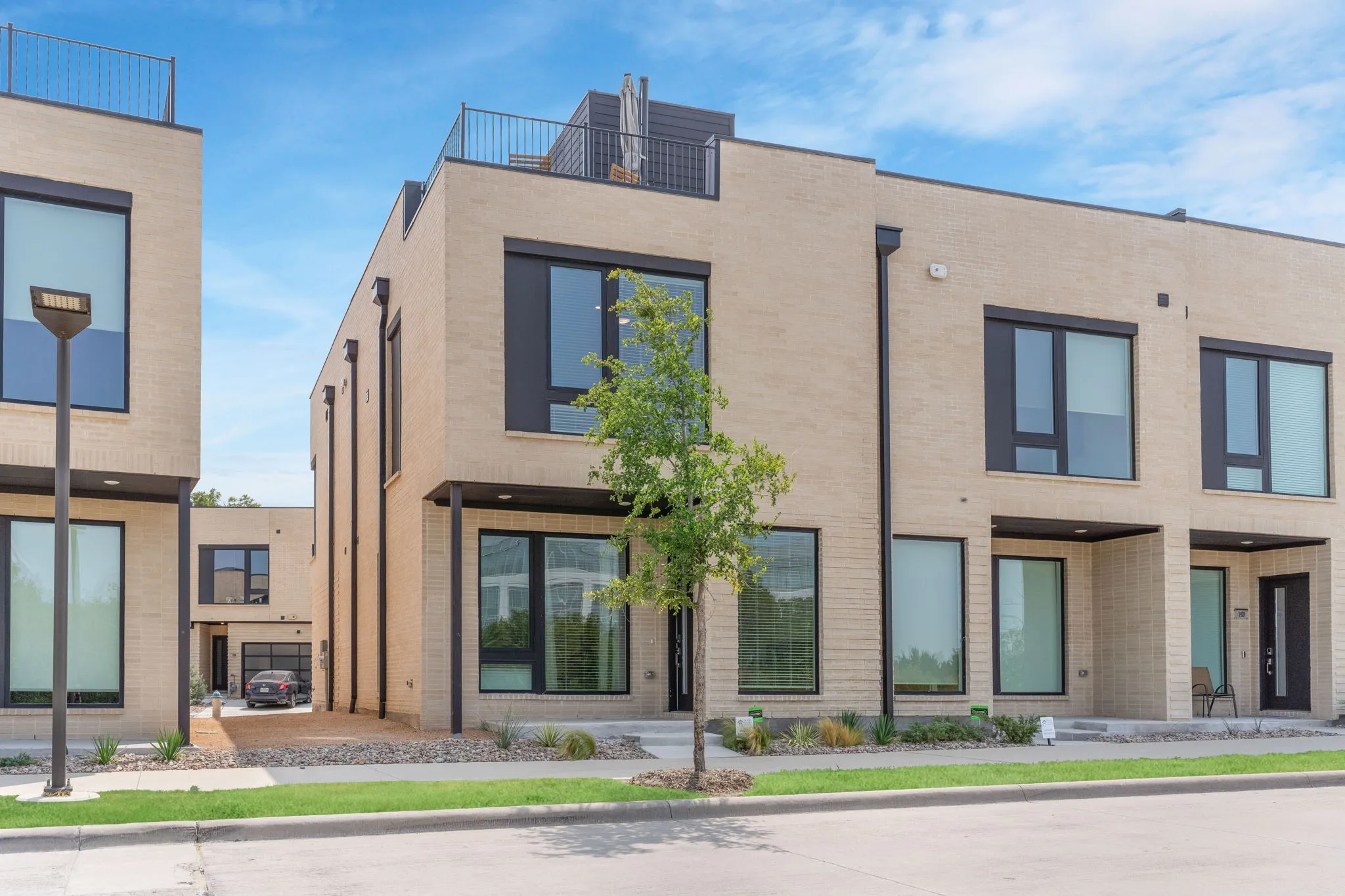 Contemporary facade featuring light-colored brick, large black-framed windows, and a flat roofline with a rooftop railing