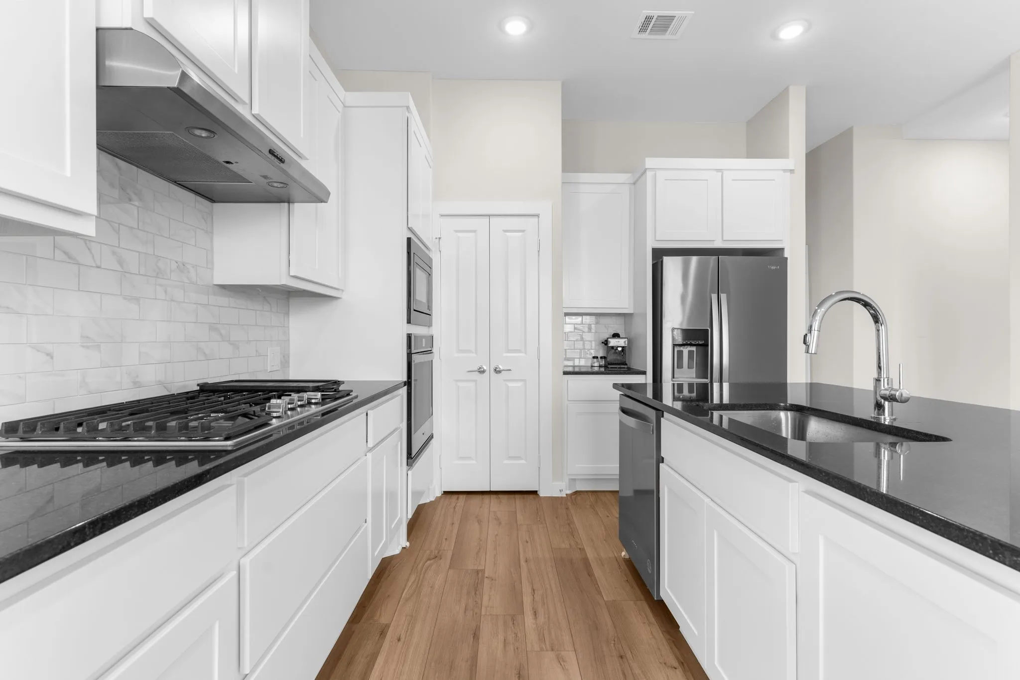 Kitchen featuring wood-finish flooring, white cabinetry, black countertops, stainless steel appliances, and a tile backsplash
