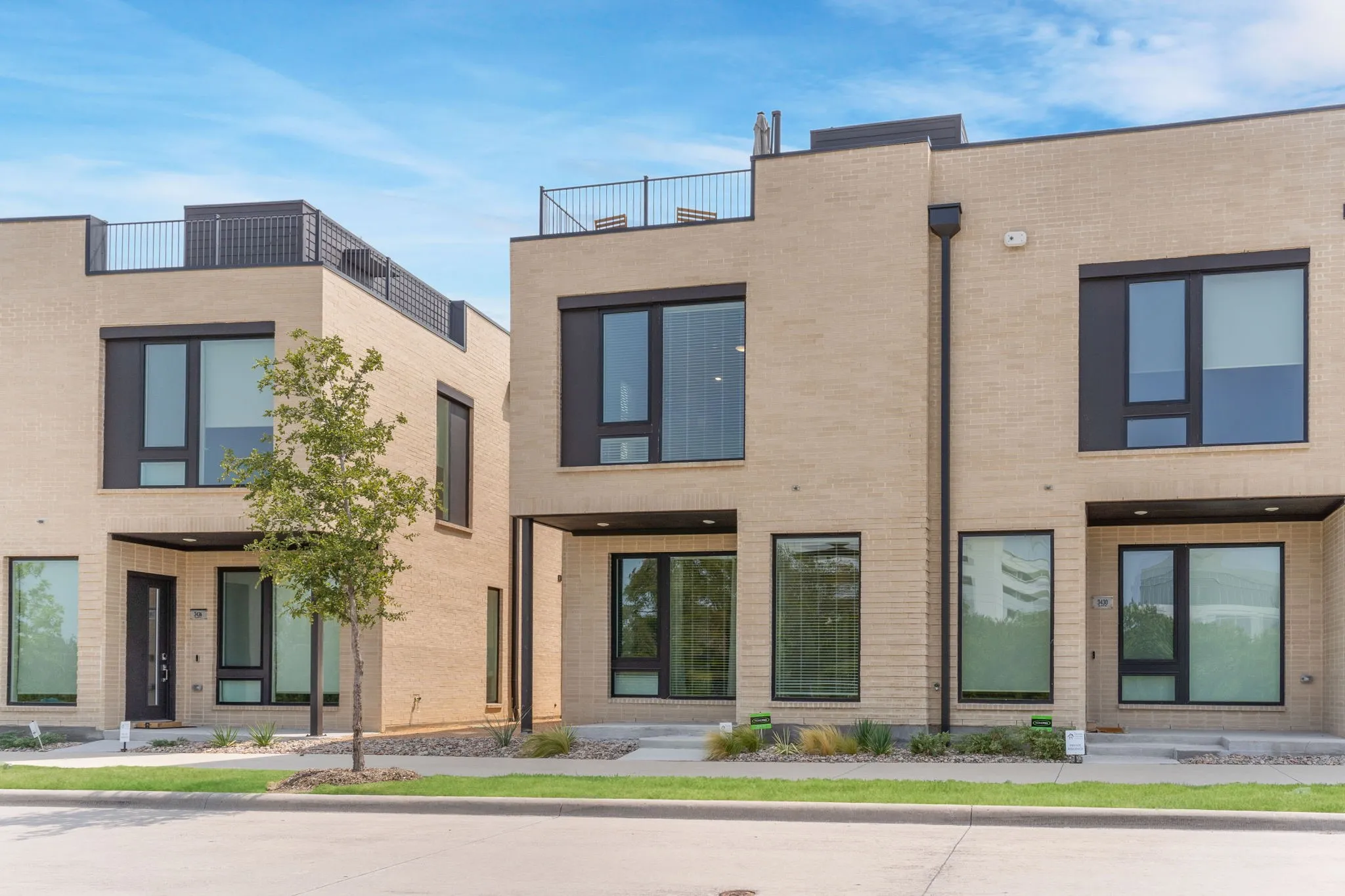 Contemporary facade featuring light-colored brick, large dark-framed windows, and rooftop terraces with metal railings