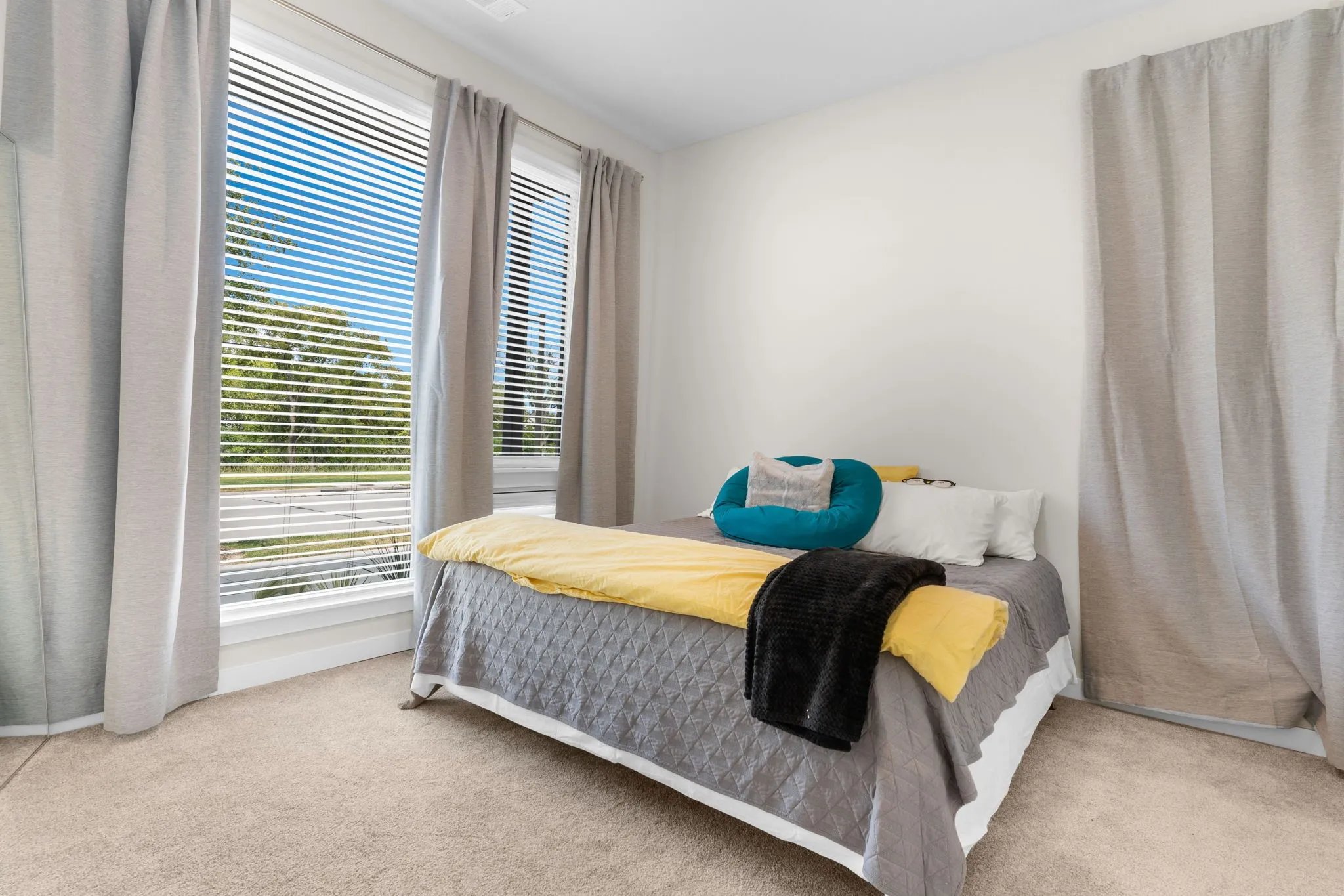 Expansive windows with blinds and drapery, neutral carpeting, and white walls