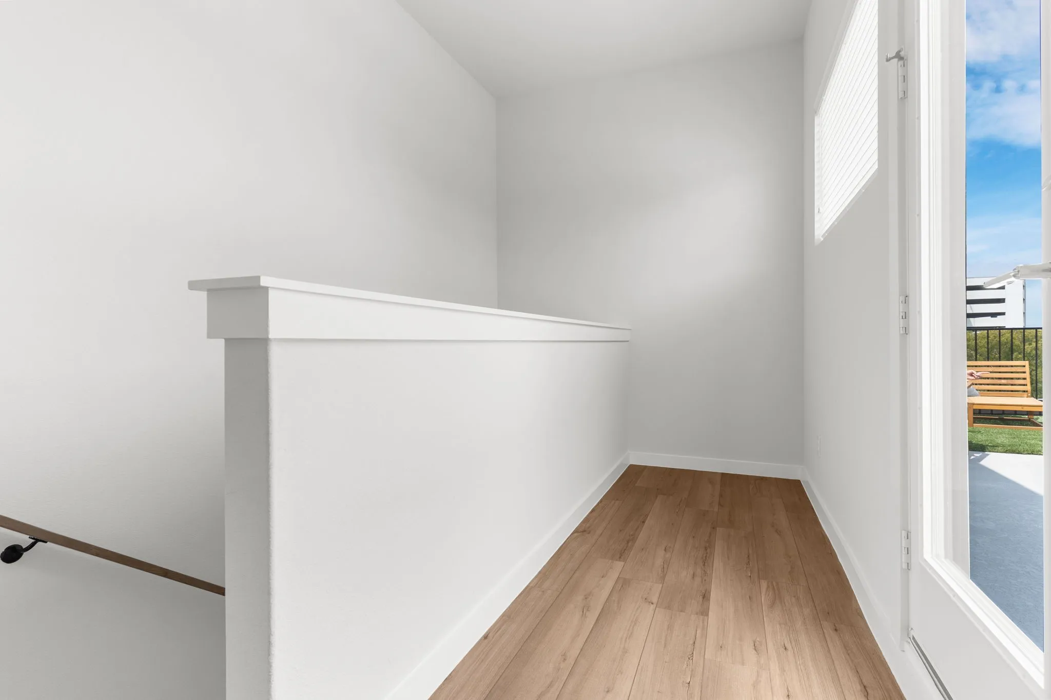 Wood-finish flooring, white walls, and a white balustrade with a wooden handrail