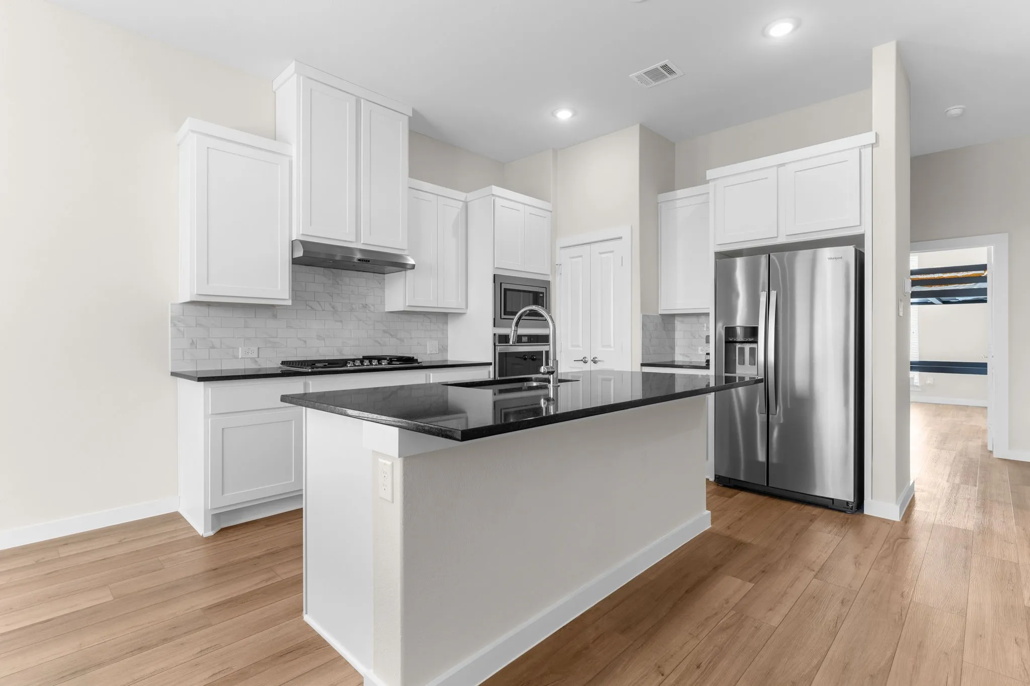 Kitchen featuring wood-finish flooring, white cabinetry, a center island with a dark countertop, white subway tile backsplash, and stainless steel appliances
