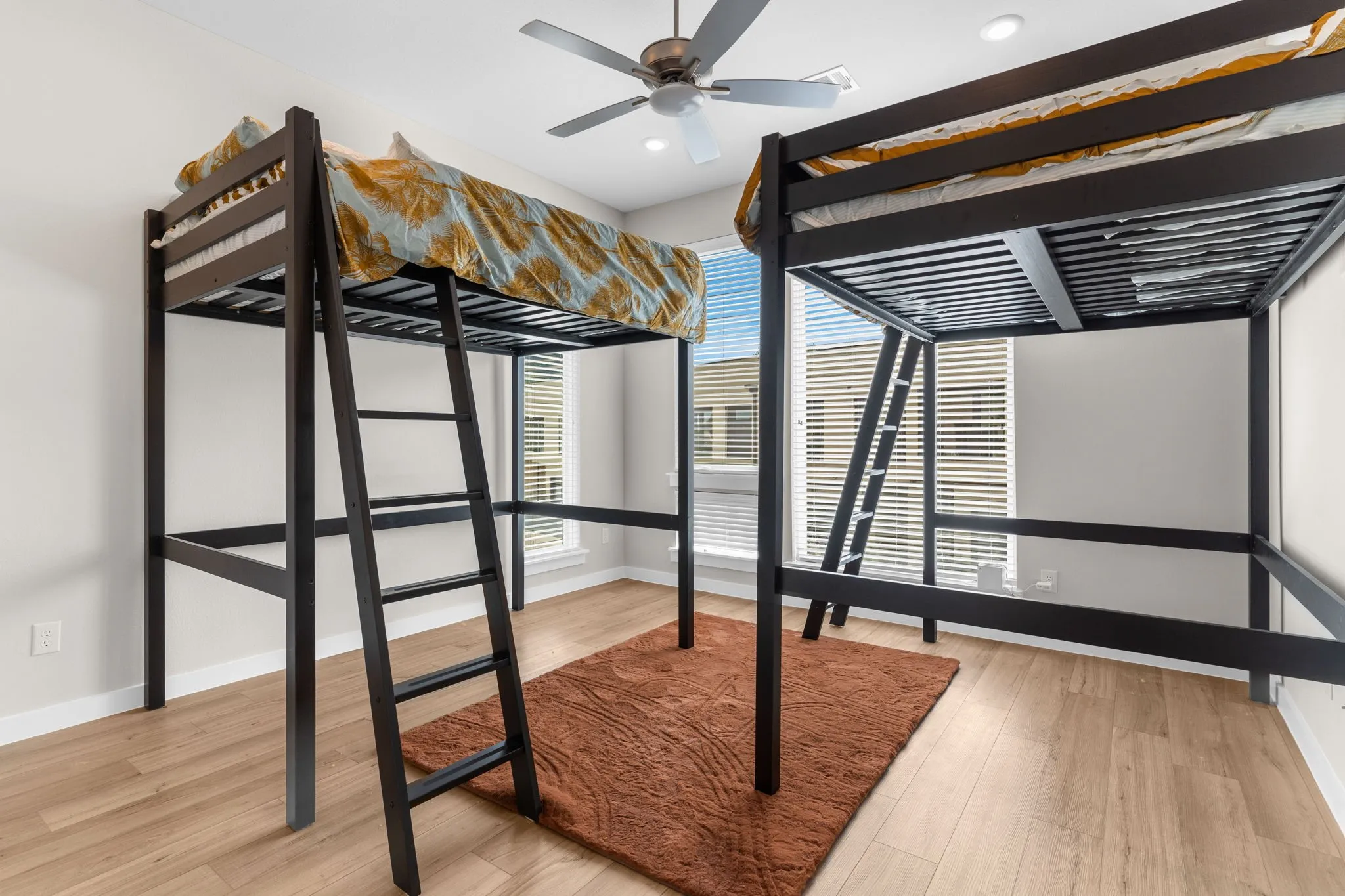 Two loft beds with dark wood frames, wood-finish flooring, recessed lighting, and a ceiling fan