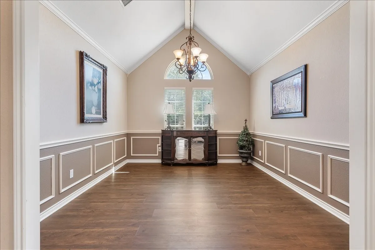 Vaulted ceiling, decorative wainscoting, wood-finish flooring, central chandelier, and arched transom window