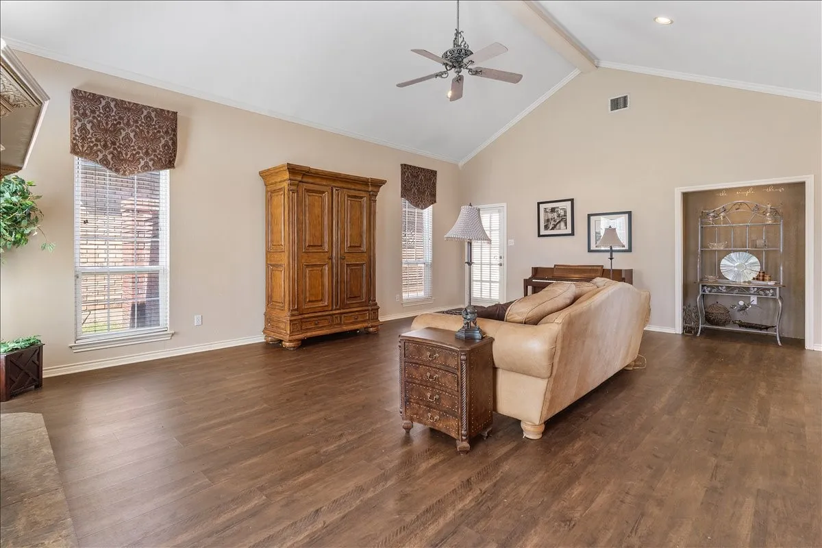 Vaulted ceiling with exposed beam, wood-finish flooring, ceiling fan, and multiple windows with blinds