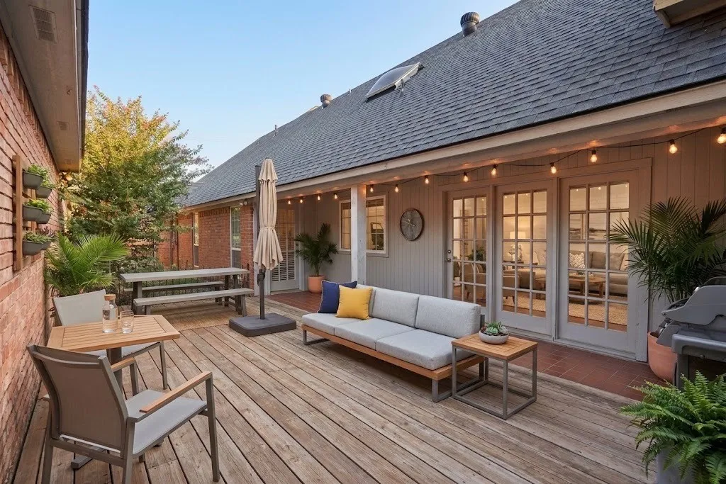 Spacious wood-finish deck with string lighting, multiple sets of French doors, and a brick exterior