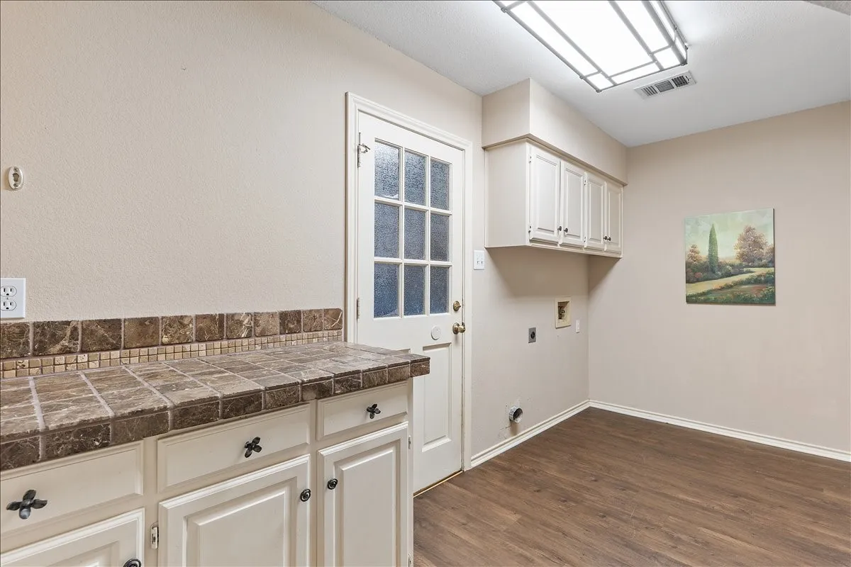 White cabinetry with decorative hardware, tiled countertop, wood-finish flooring, and a glass-paneled door
