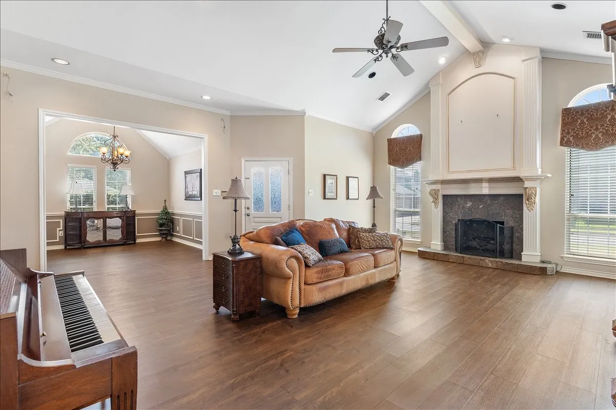 Vaulted ceiling with exposed beam, wood-finish flooring, recessed lighting, fireplace with stone surround, and decorative archway