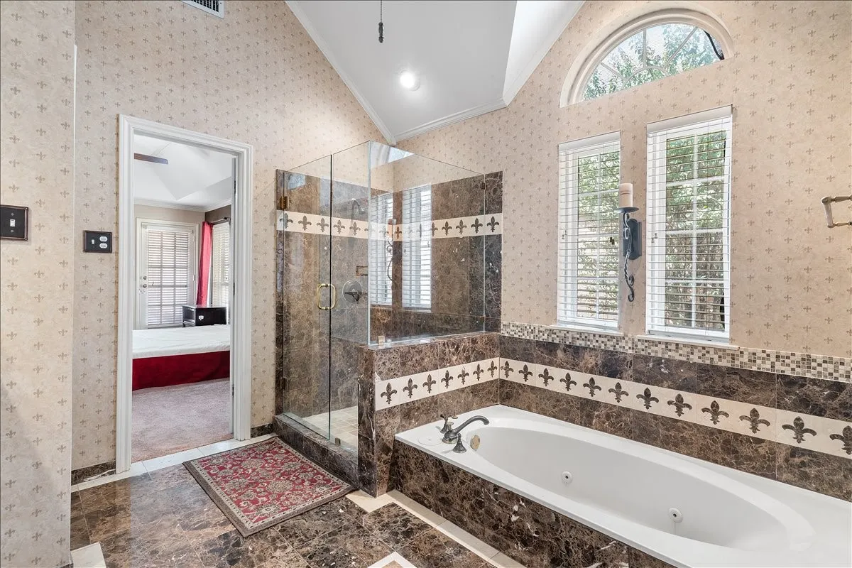 Vaulted ceiling bathroom featuring a jetted soaking tub, glass-enclosed shower, and arched transom window