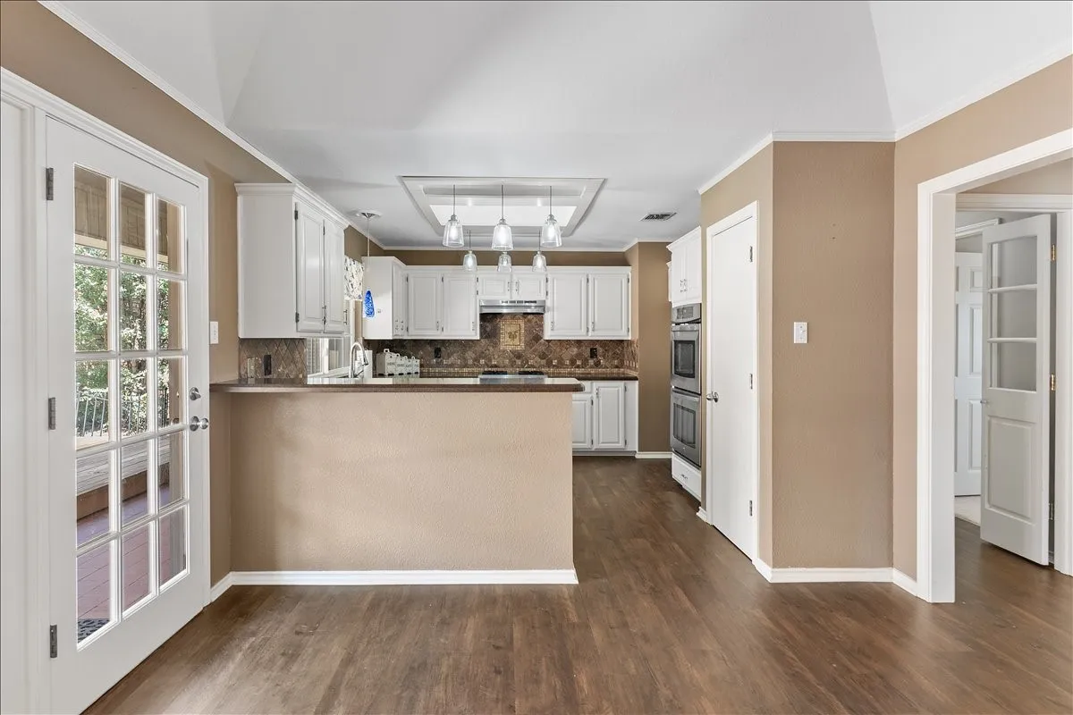 Kitchen with white cabinetry, wood-finish flooring, built-in double ovens, and a central island with pendant lighting