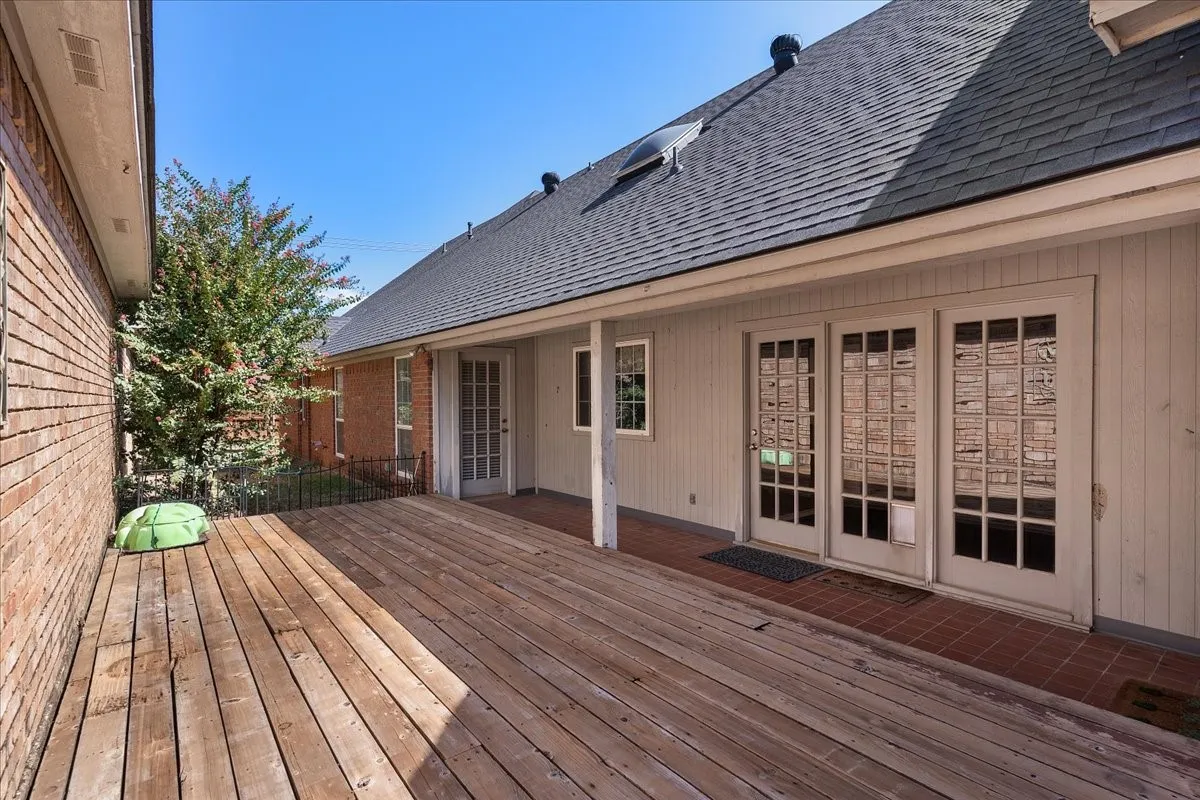 Expansive wood-finish deck with multiple French-style doors, covered patio, and brick exterior