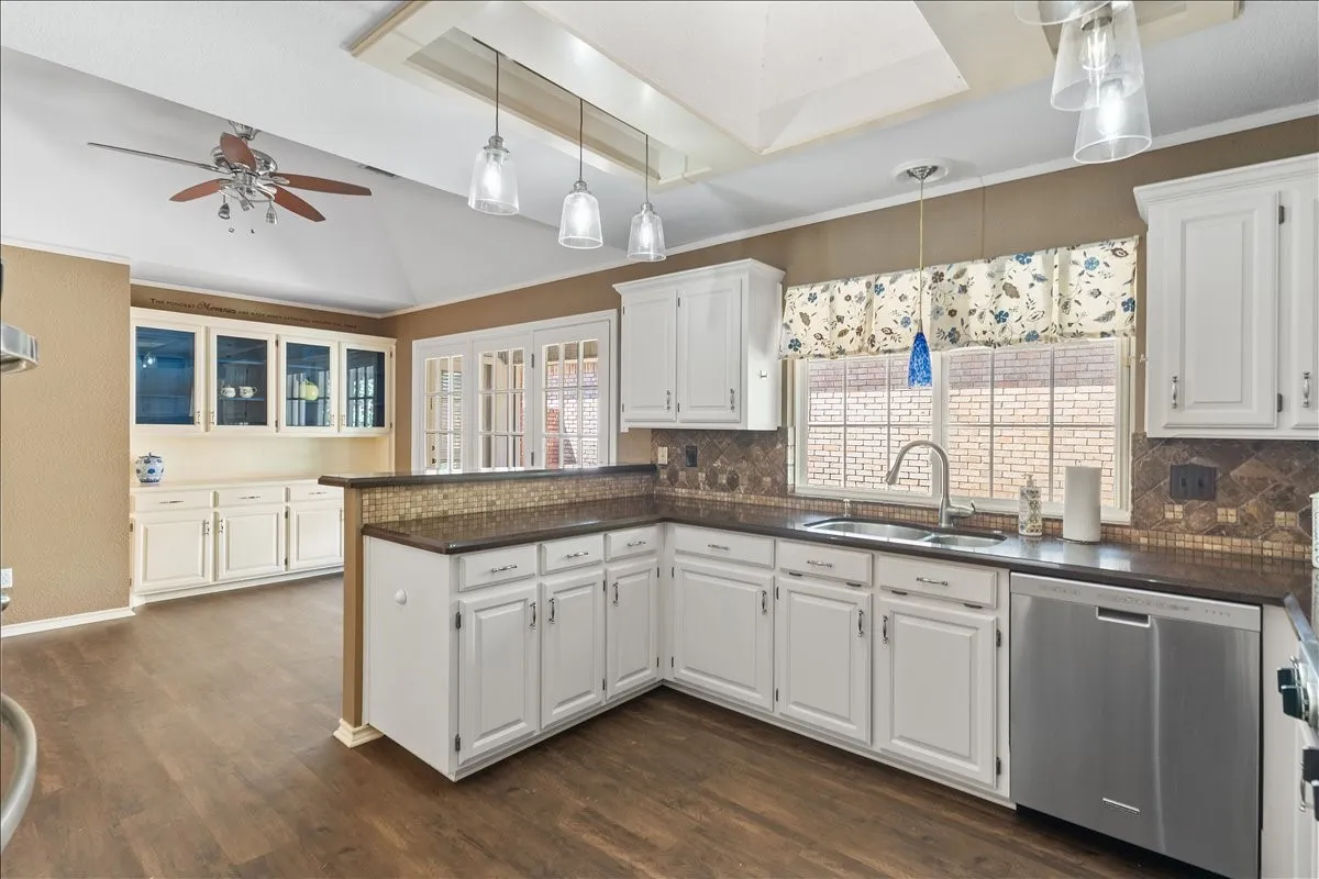 White cabinetry, stainless steel appliances, wood-finish flooring, vaulted ceiling, and built-in display cabinetry