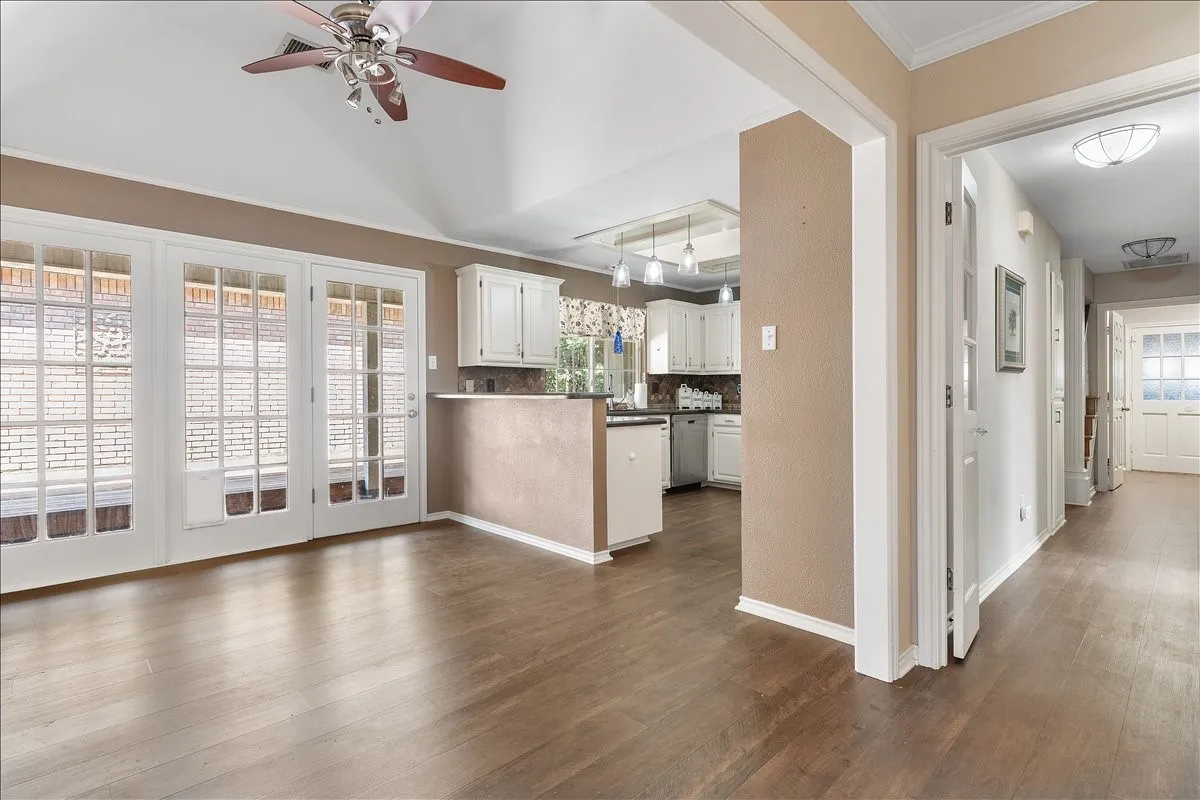 Vaulted ceiling with a ceiling fan, French doors, wood-finish flooring, and white cabinetry