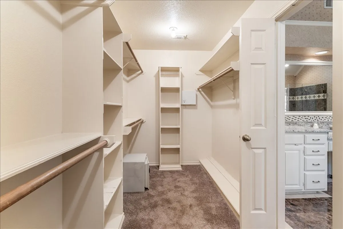 Carpeted walk-in closet featuring multiple shelving units and hanging rods