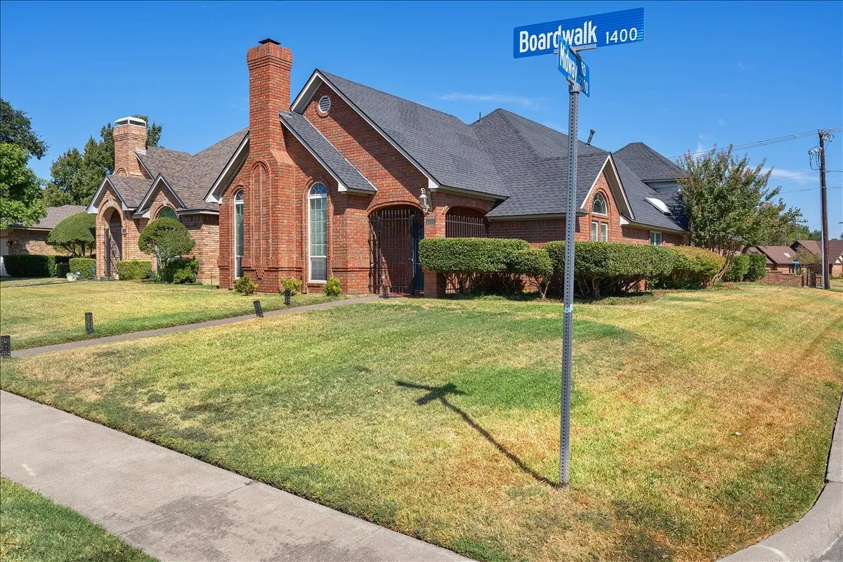 Brick exterior featuring a prominent chimney, dark shingled roof, and manicured shrubbery