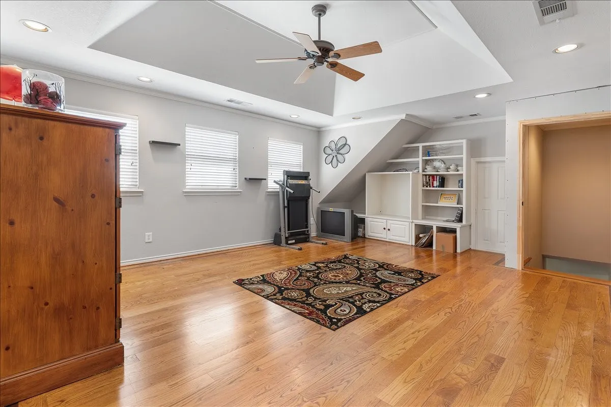 Hardwood-finish flooring throughout, tray ceiling with a ceiling fan, recessed lighting, and built-in shelving