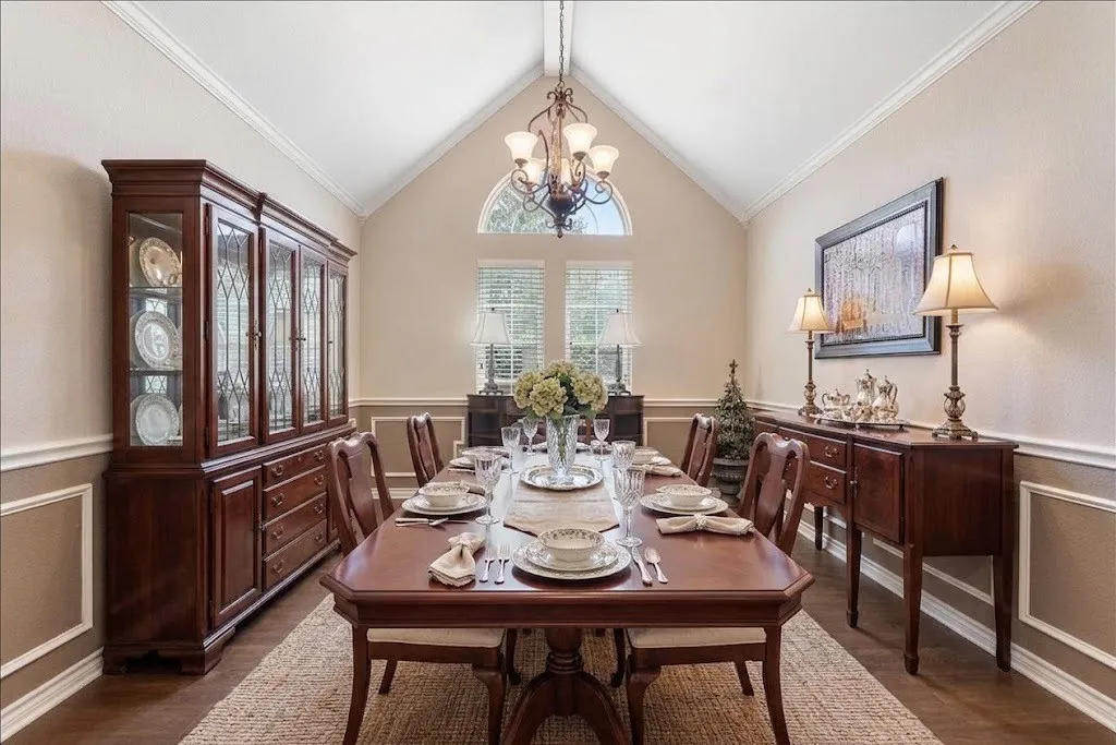 Vaulted ceiling with a chandelier, wood-finish flooring, half-wall wainscoting, and an arched window