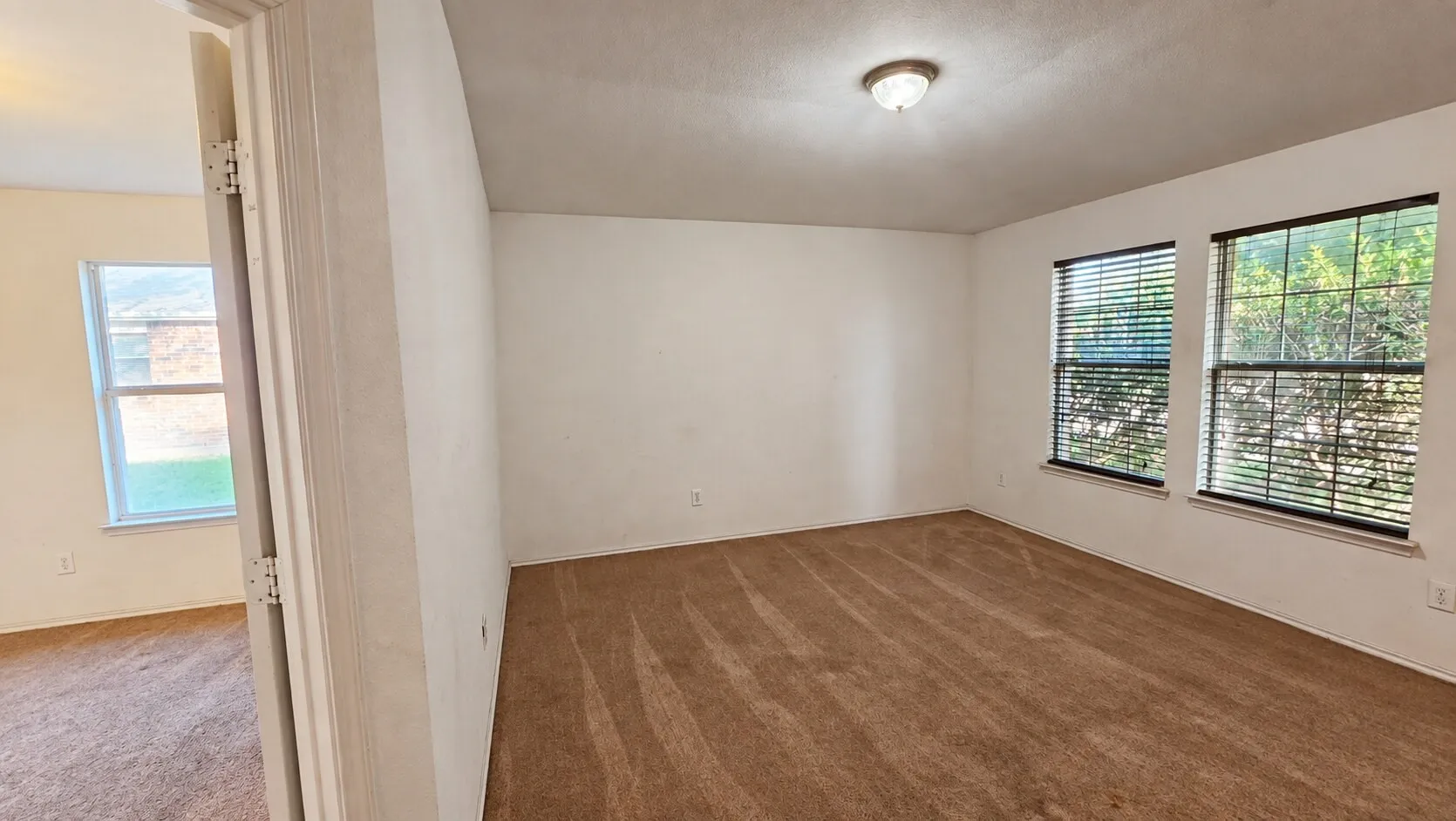 Neutral wall color, carpet flooring, two windows with blinds, and a flush-mount ceiling light fixture