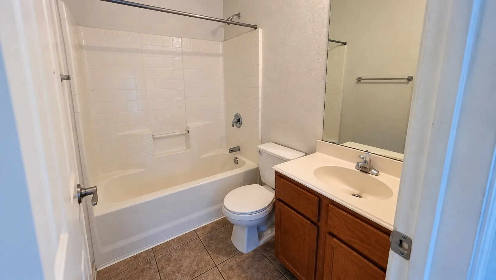 Bathroom featuring a built-in bathtub with shower, wood-finish vanity with an integrated sink, wall-mounted mirror, and tile flooring