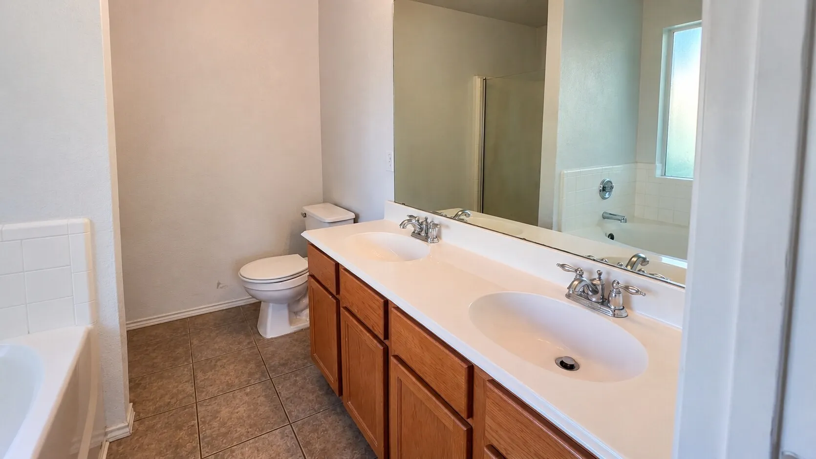 Dual vanity with wood-finish cabinetry, integrated sinks, and chrome faucets