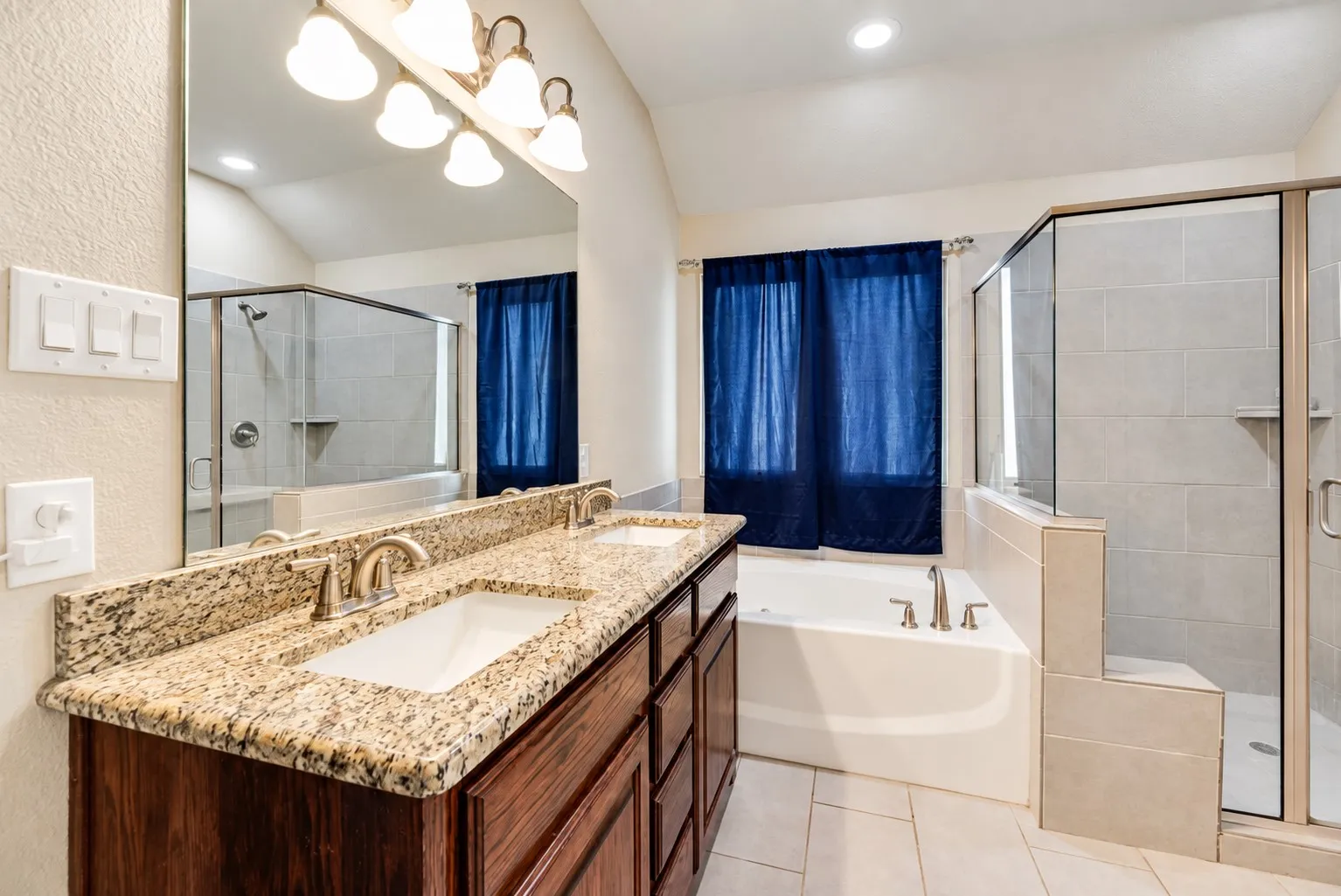 Dual vanity with granite-style countertop, built-in soaking tub, and glass-enclosed shower with tile surround