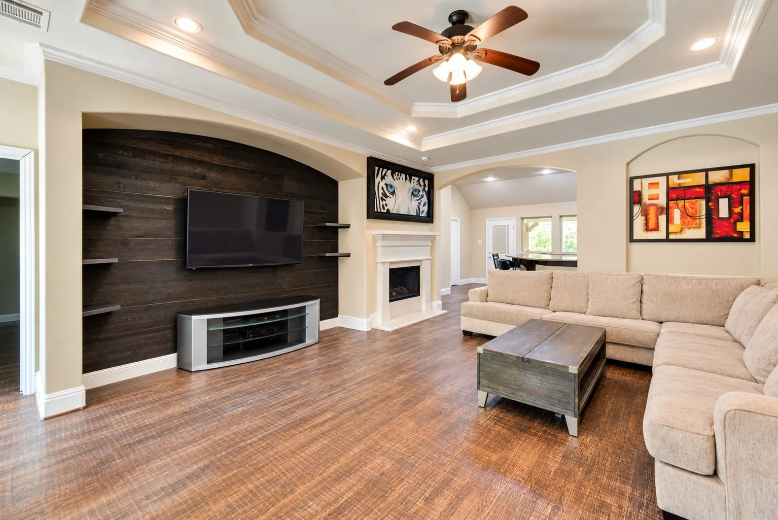 Wood-finish flooring, recessed lighting, ceiling fan, decorative tray ceiling, and a fireplace with mantle