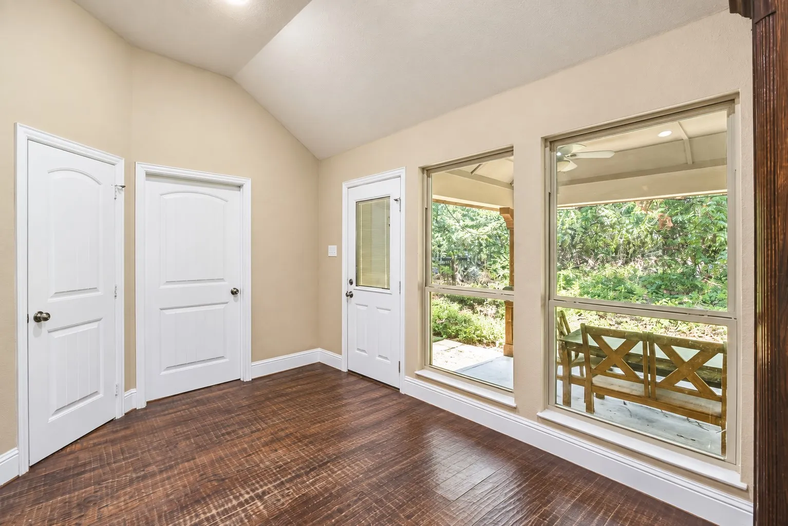 Wood-finish flooring, vaulted ceiling, white trim, and direct access to an outdoor patio with a ceiling fan