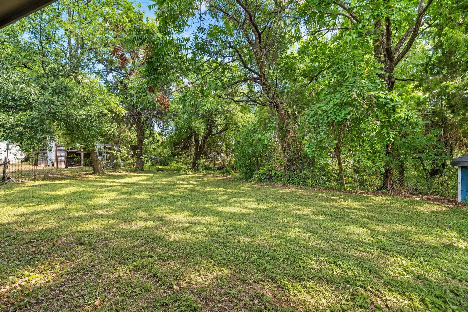Expansive lawn area with mature trees and a chain-link fence